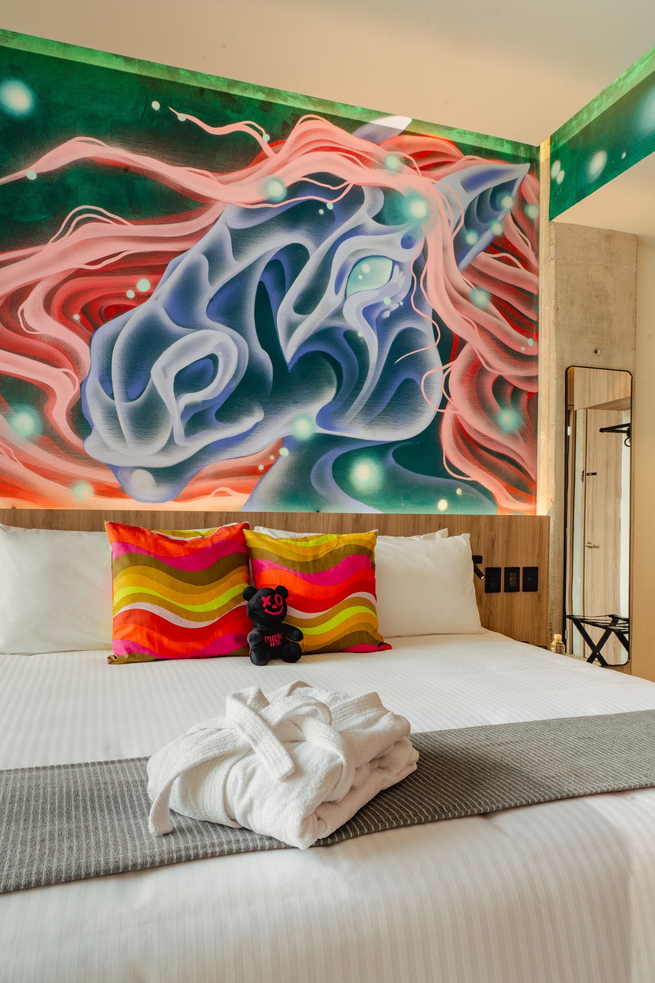 Bedroom with a colorful horse mural, bed with pillows, robe, and a mirror.