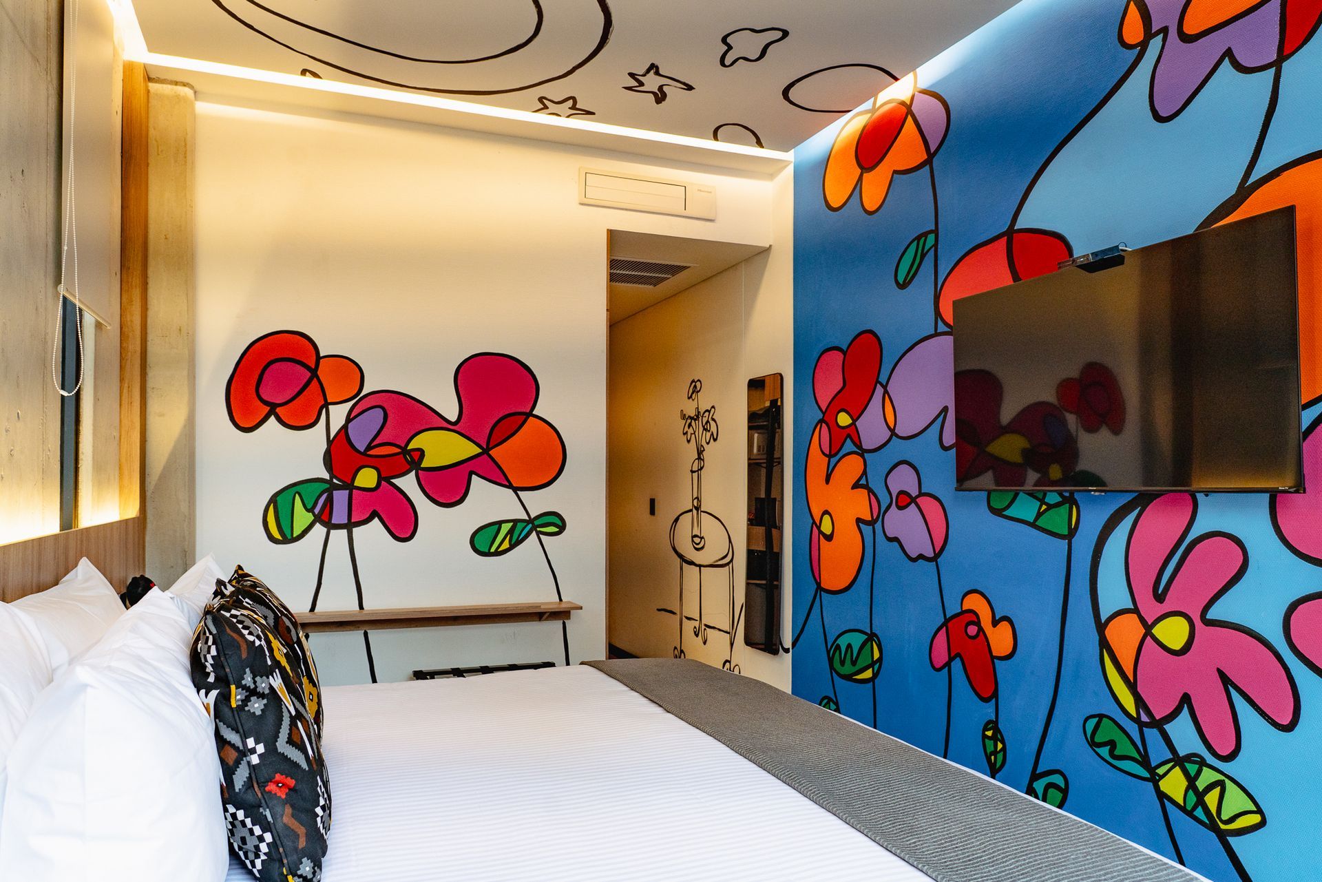 Brightly painted hotel room with floral mural, bed, and TV.