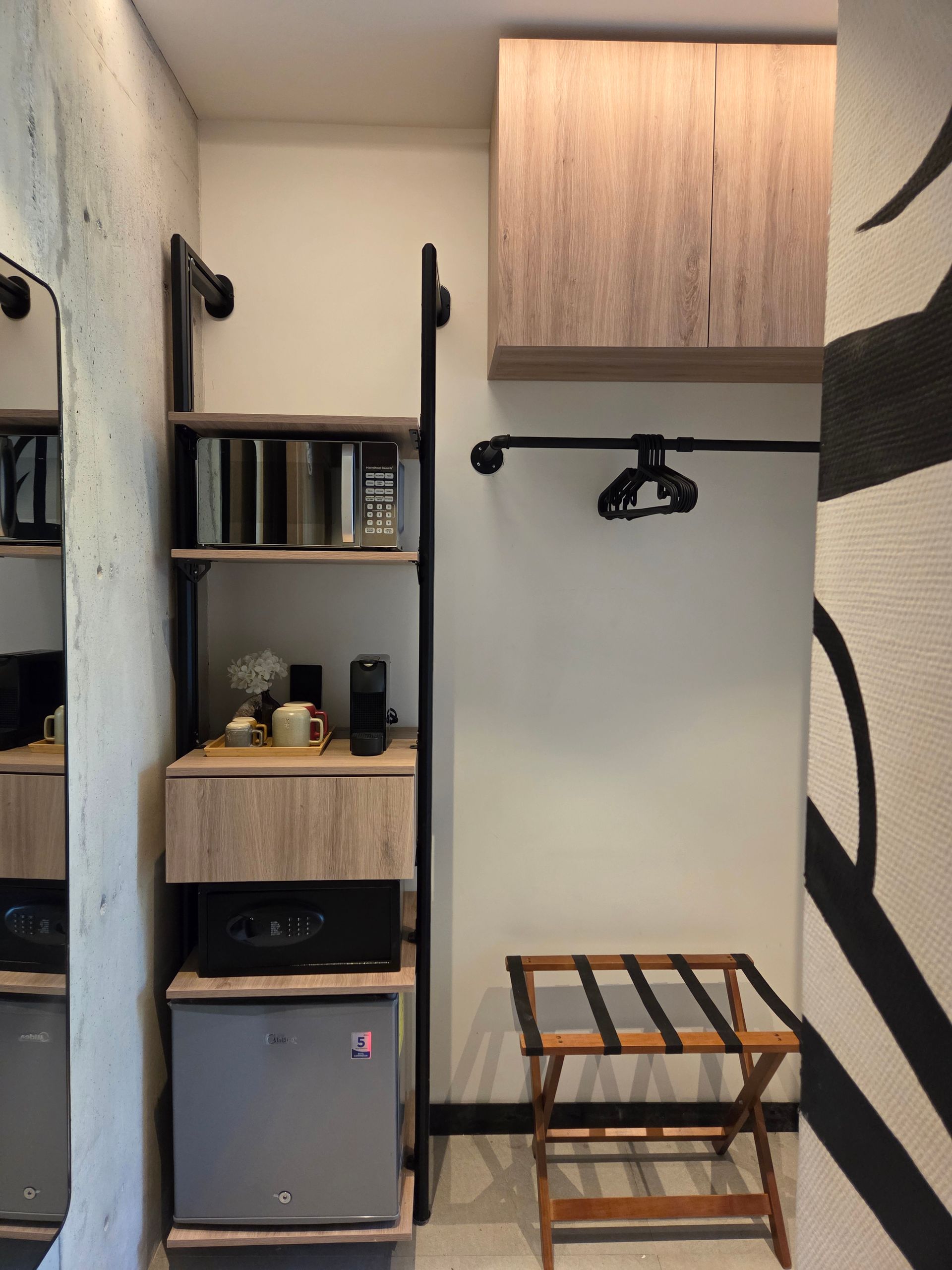 Hotel room nook with shelves, mini-fridge, luggage rack, hanging rod, and cabinet.