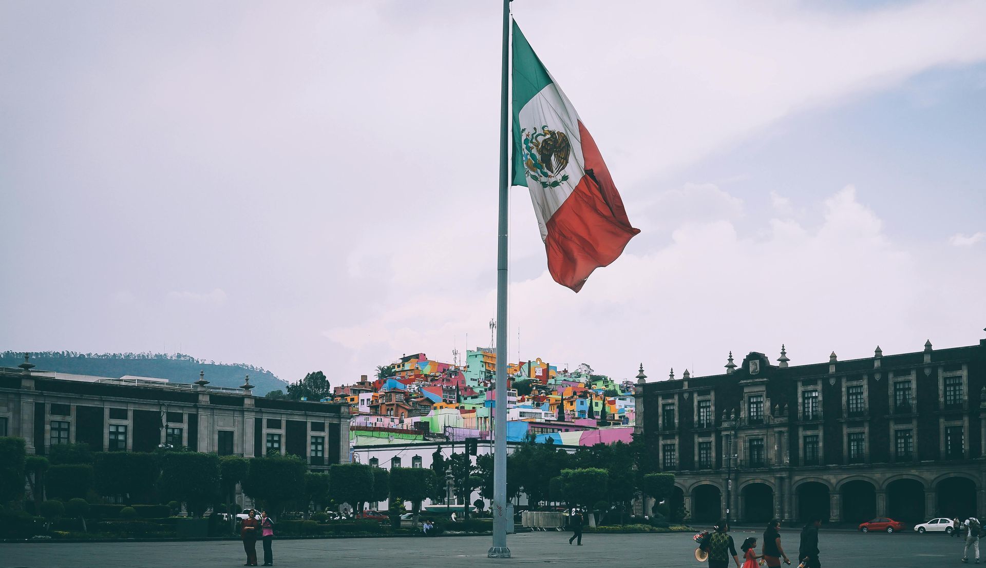 A mexican flag is flying in the wind in front of a building.