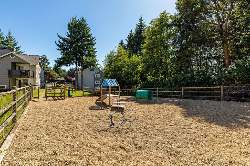 Playground with wood chips, small slide, tunnel, and low fence.