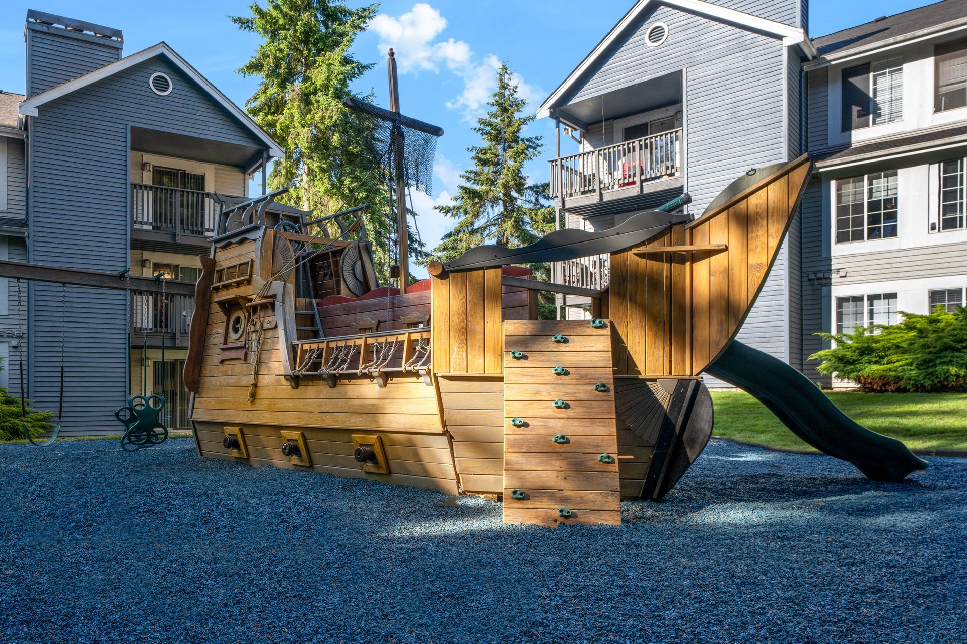 A wooden pirate ship playground with a slide in front of a building.