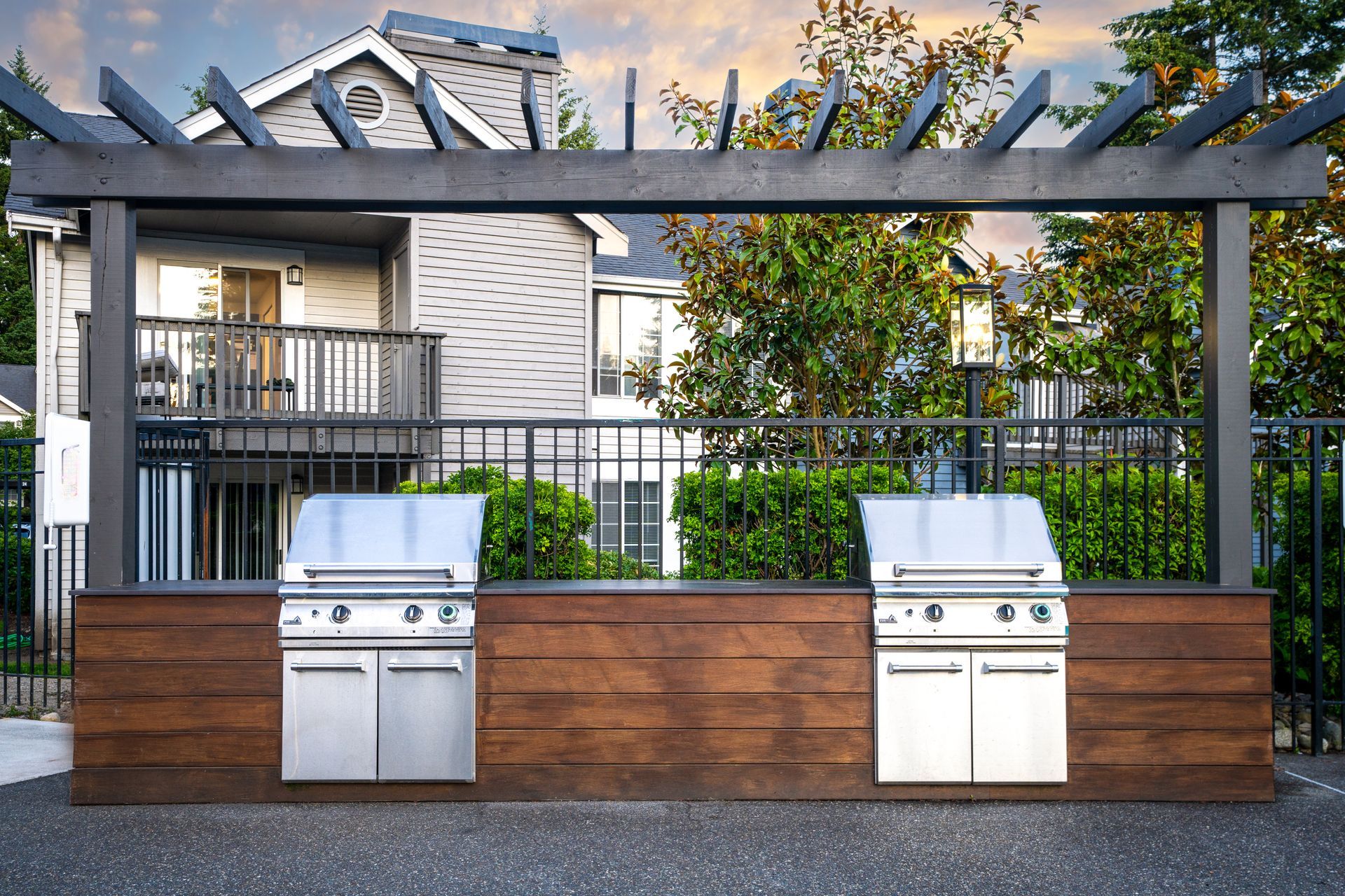 A bbq grill is sitting under a pergola in front of a house.