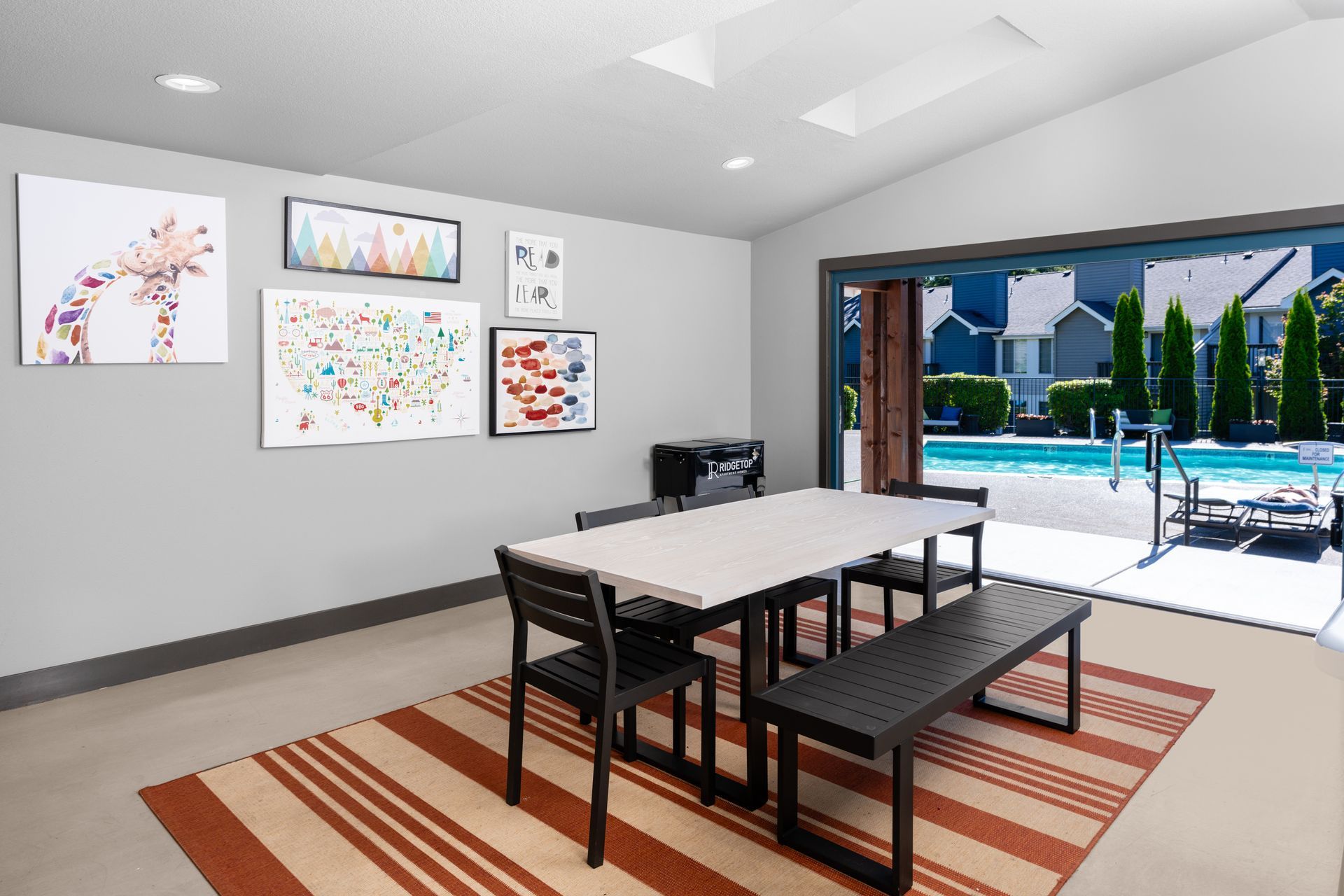 A dining room with a table and chairs and a swimming pool in the background.