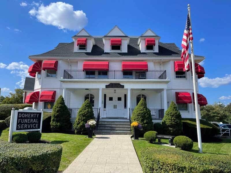 Red-roofed funeral home with white columns and American flag under a blue sky