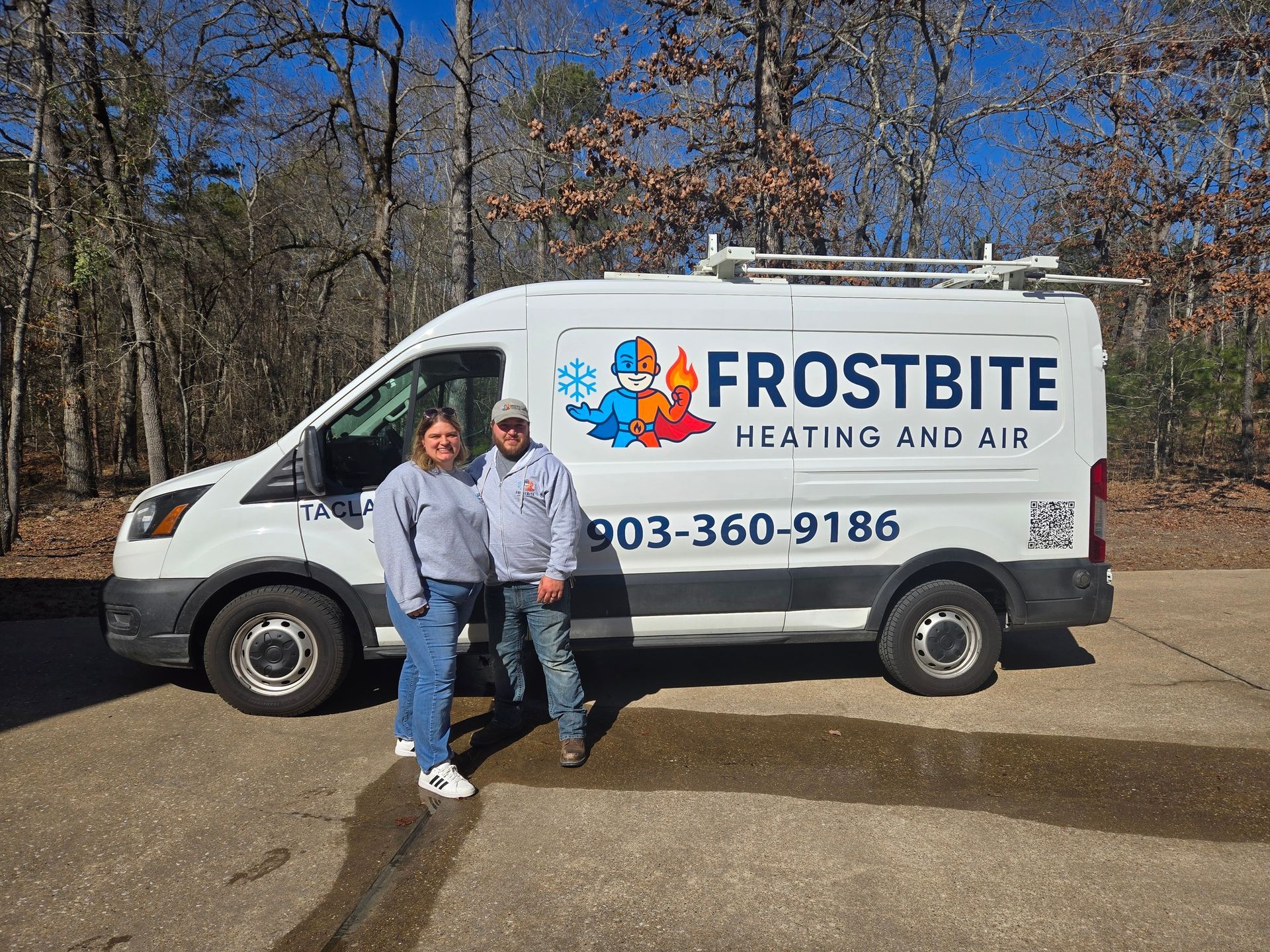 Two people standing beside a Frostbite Heating and Air service van outdoors.