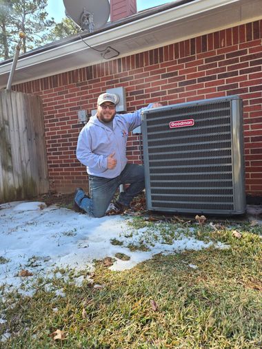 Person kneeling beside a large outdoor HVAC unit against a brick wall on a snowy day.