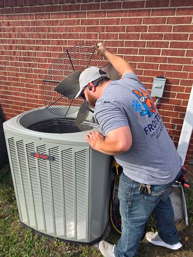 Technician repairing outdoor air conditioner unit beside a brick wall