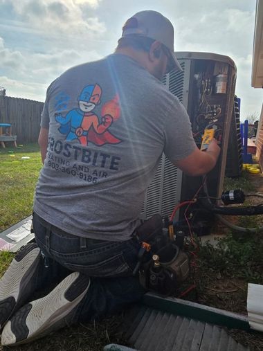 Technician kneeling beside an outdoor HVAC unit, working on exposed wiring in a grassy yard.