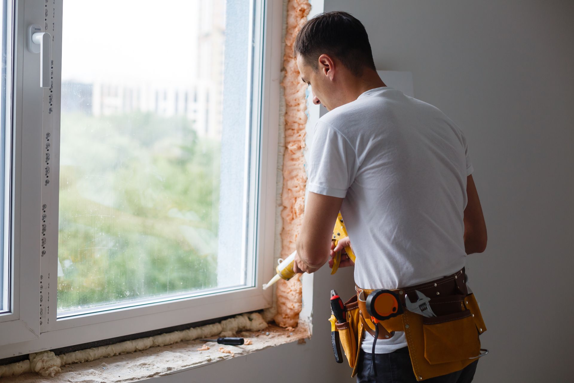 Person applying sealant around a window frame with a caulk gun.