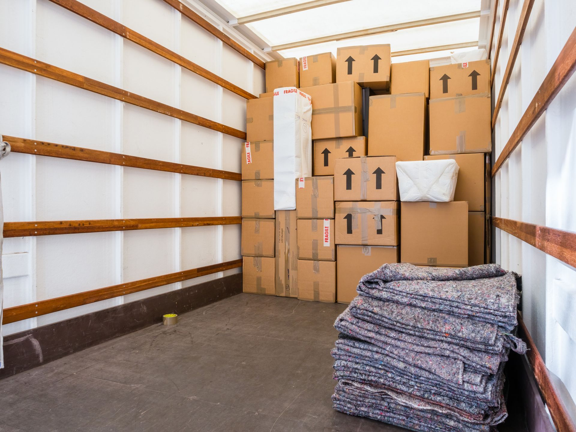 Interior of a moving truck filled with stacked cardboard boxes and protective moving blankets.
