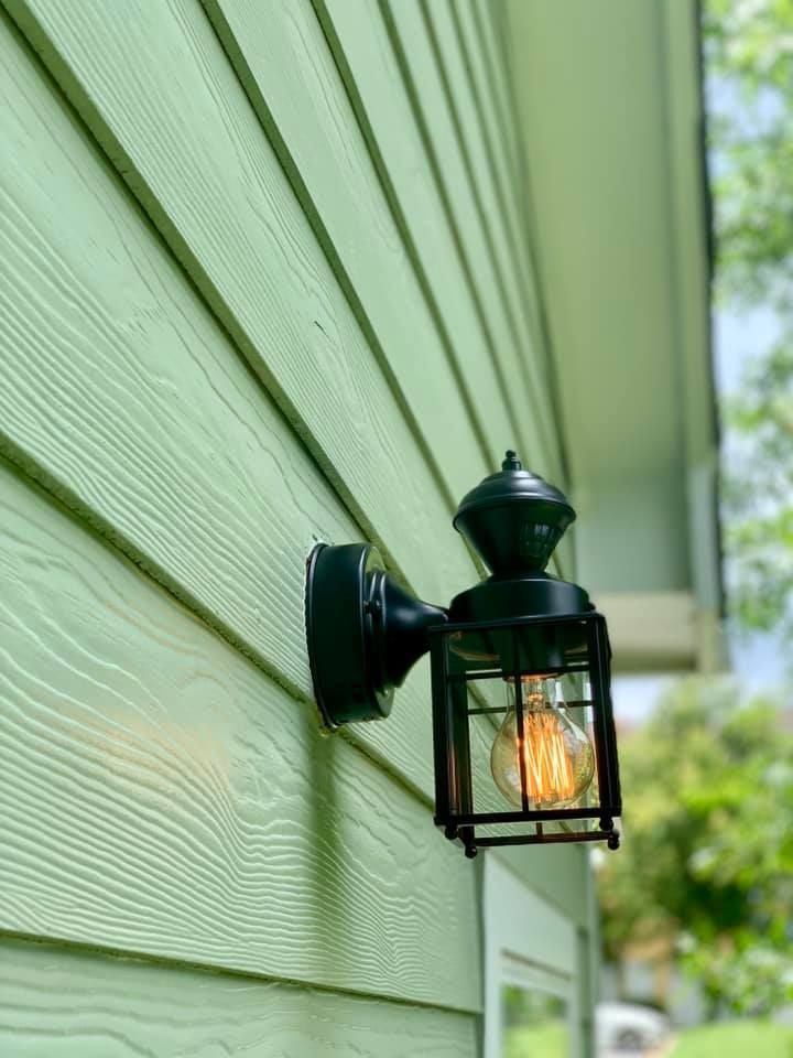 A light is hanging on the side of a green house.