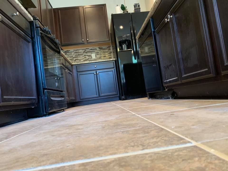 A kitchen with brown cabinets , black appliances , and a tiled floor.