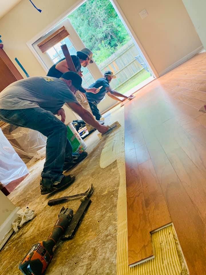 A group of men are working on a hardwood floor in a living room.