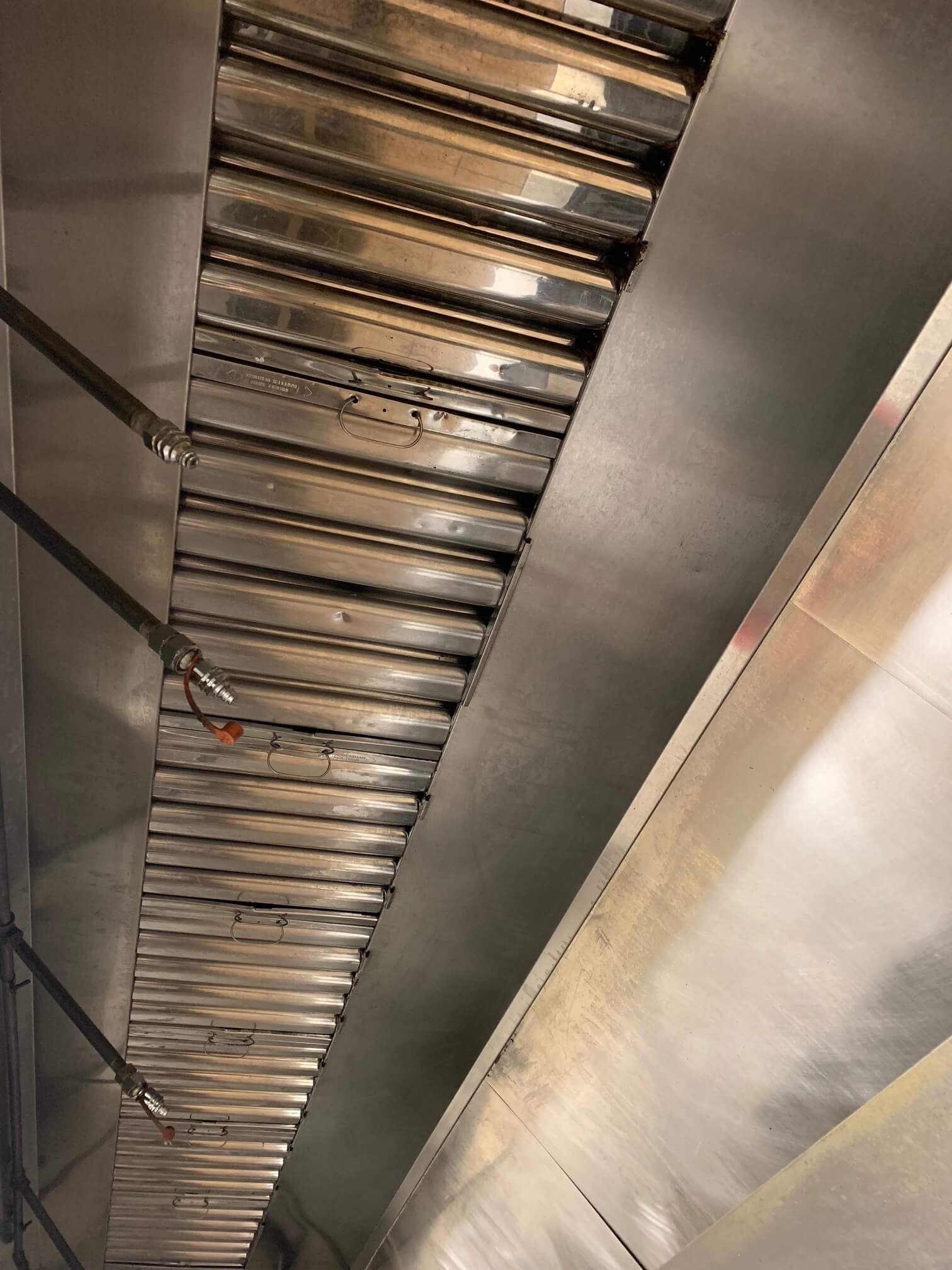 A stainless steel exhaust hood is hanging from the ceiling of a kitchen.