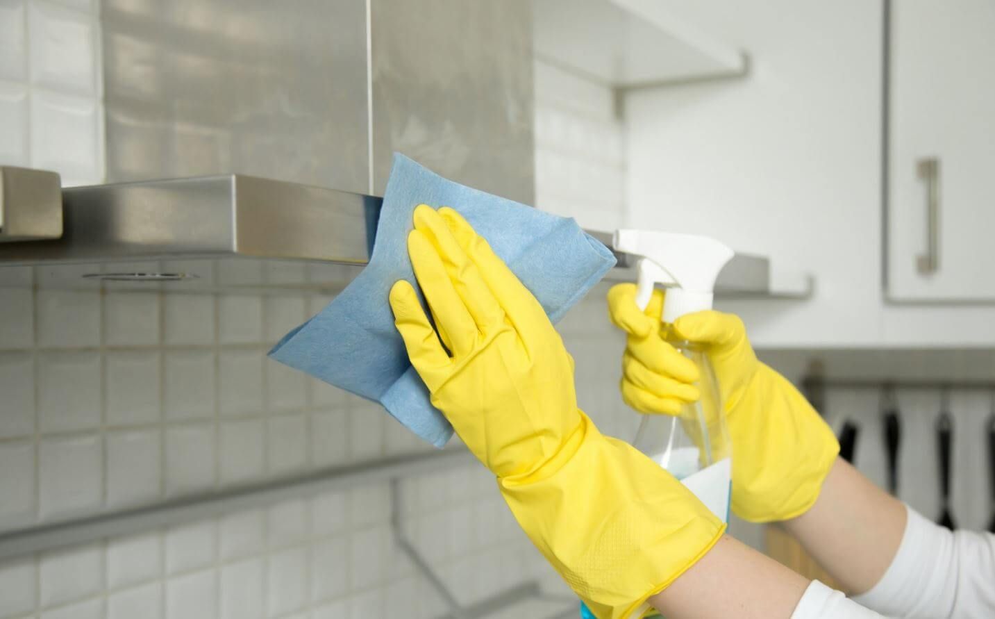 A person wearing yellow gloves is cleaning a stainless steel hood.