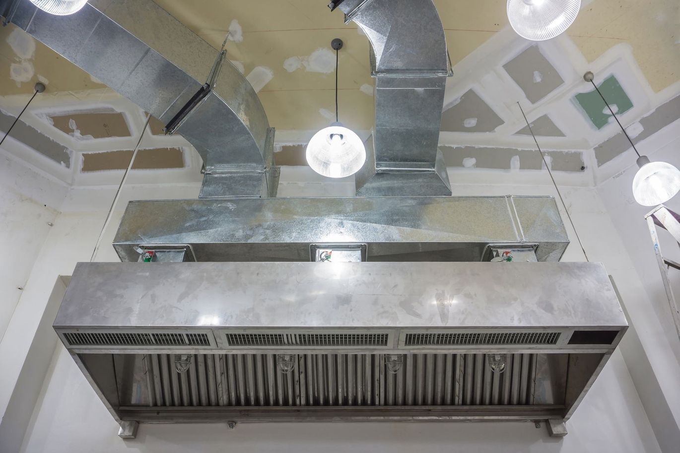 A stainless steel hood is hanging from the ceiling in a kitchen.