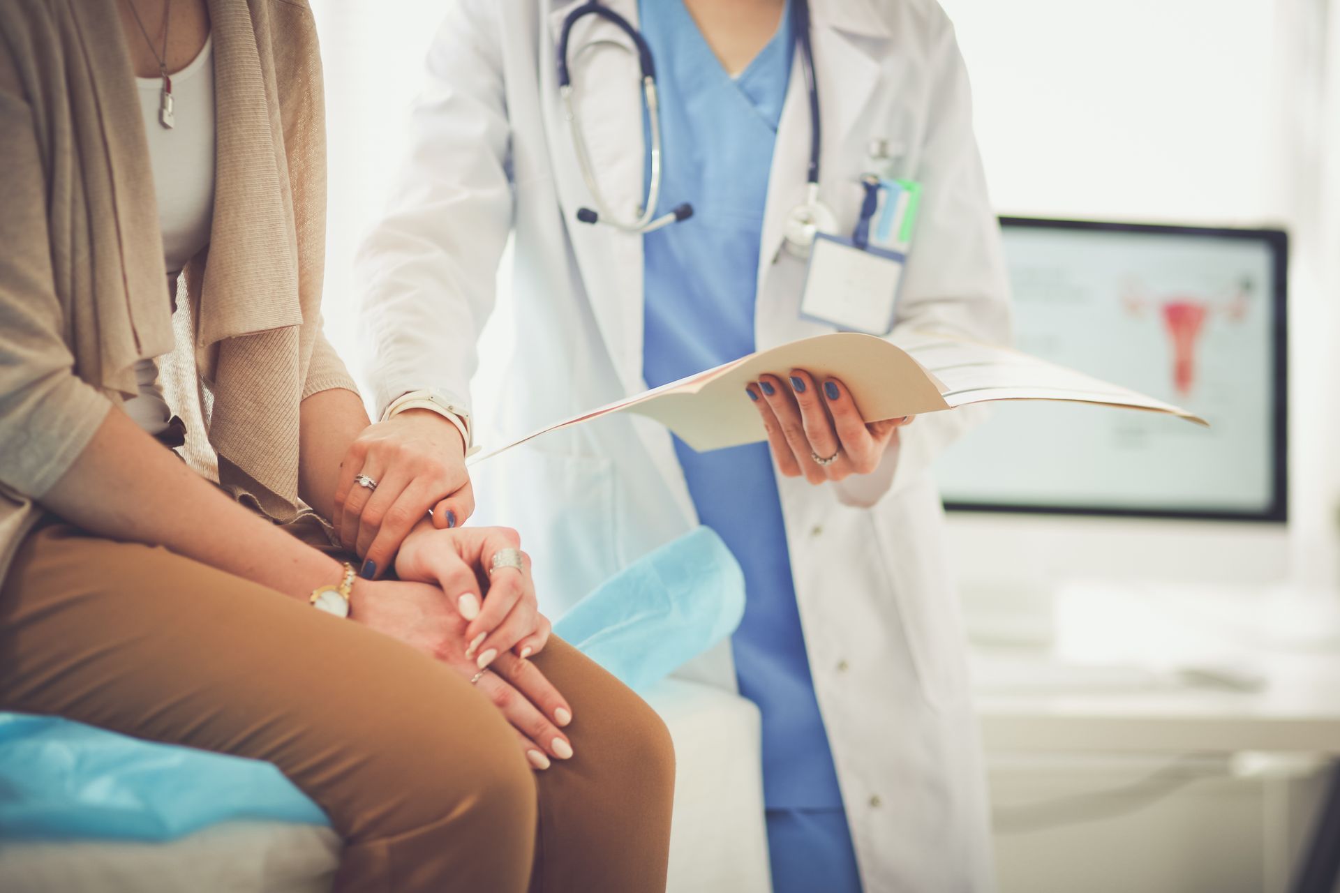 A doctor is holding the hand of a patient while looking at a clipboard.