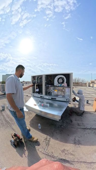 Two workers service a large HVAC unit on a sunny rooftop.