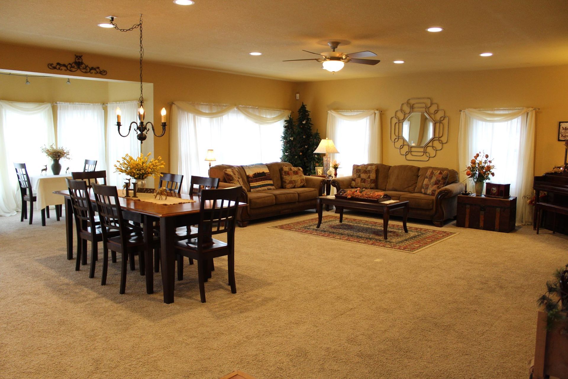 A spacious, well-lit living and dining room with neutral carpet, a dark wood dining table, and two brown fabric sofas.