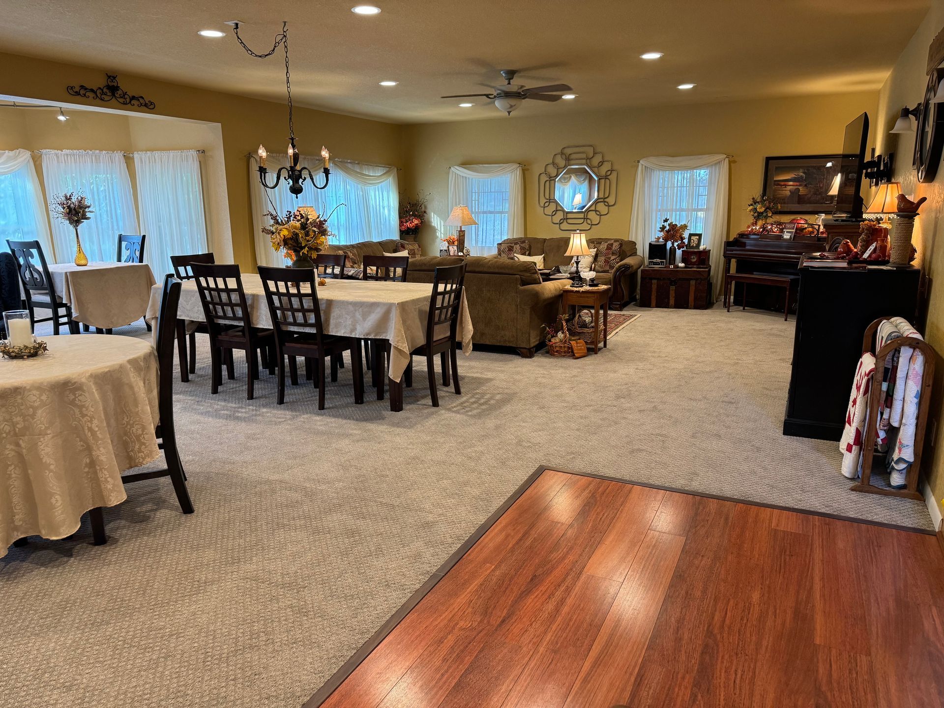 A spacious, neutrally toned living and dining room with carpet flooring and hardwood in the foreground.