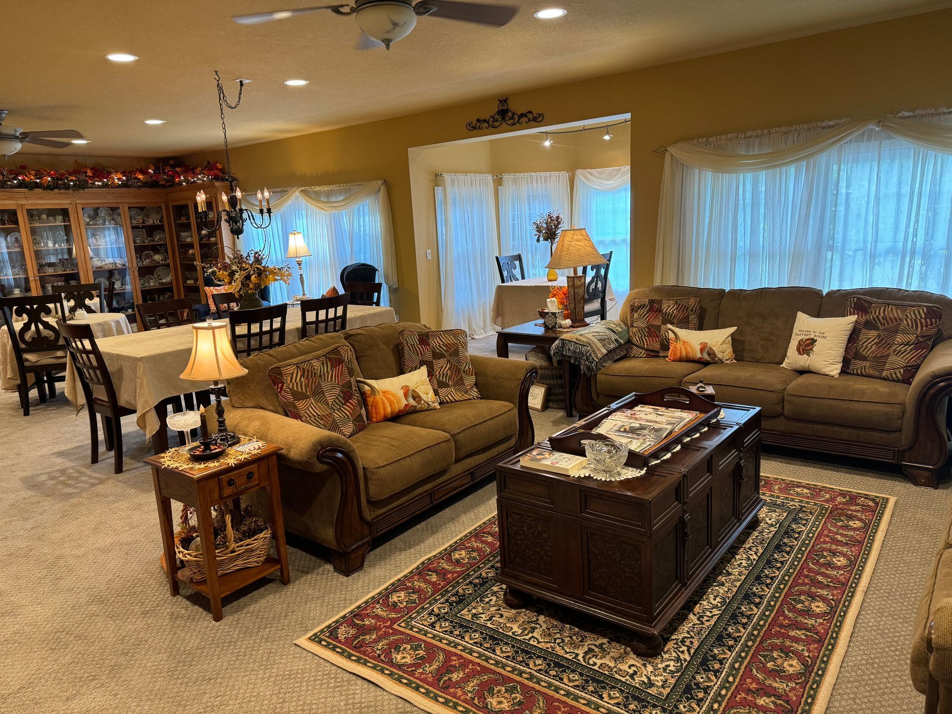 A living room featuring a brown sofa, a patterned rug, a wooden trunk coffee table, and an adjacent dining area.