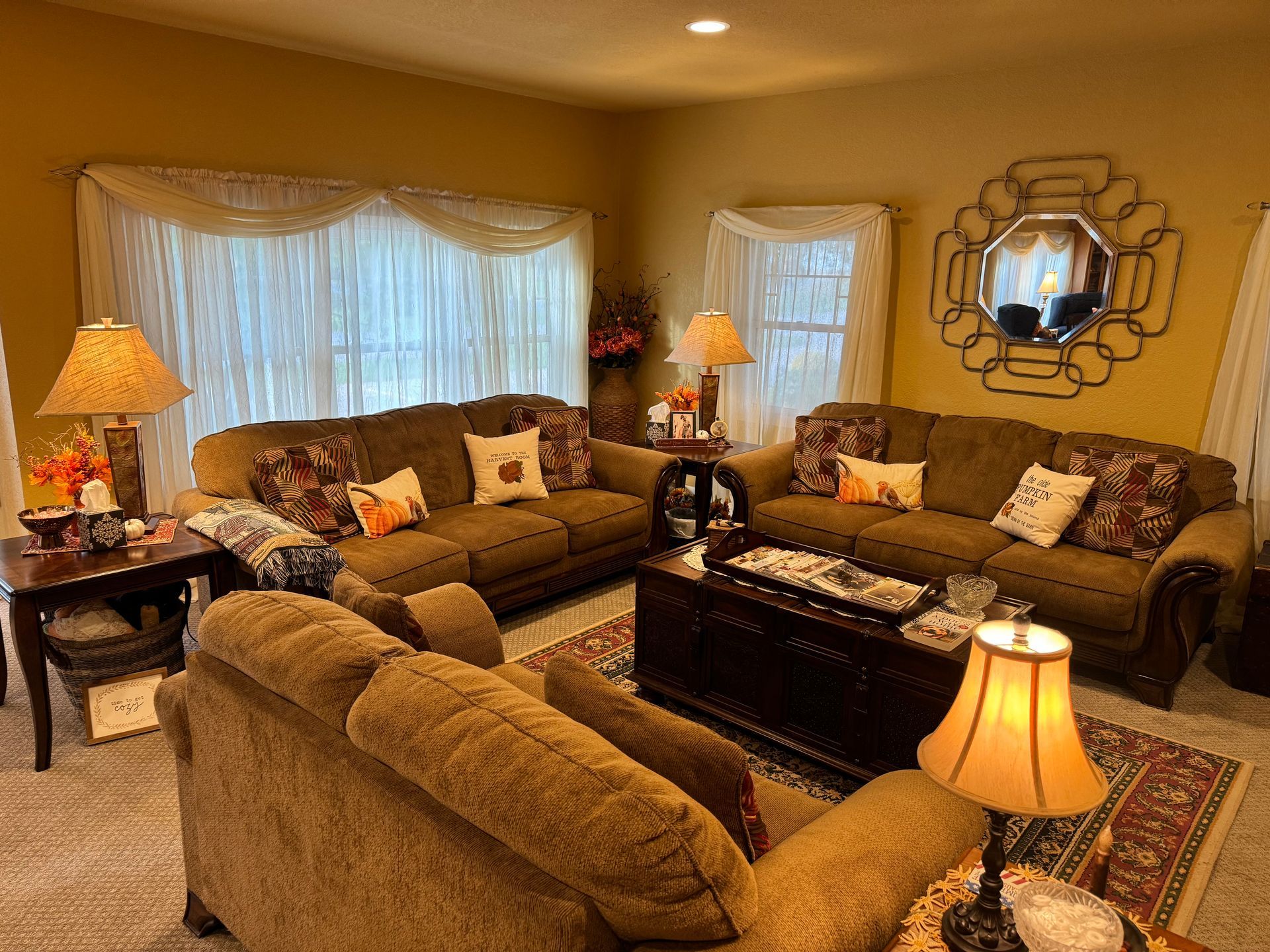 A cozy living room with brown sofas, a wooden coffee table, decorative lamps, and a unique wall mirror.