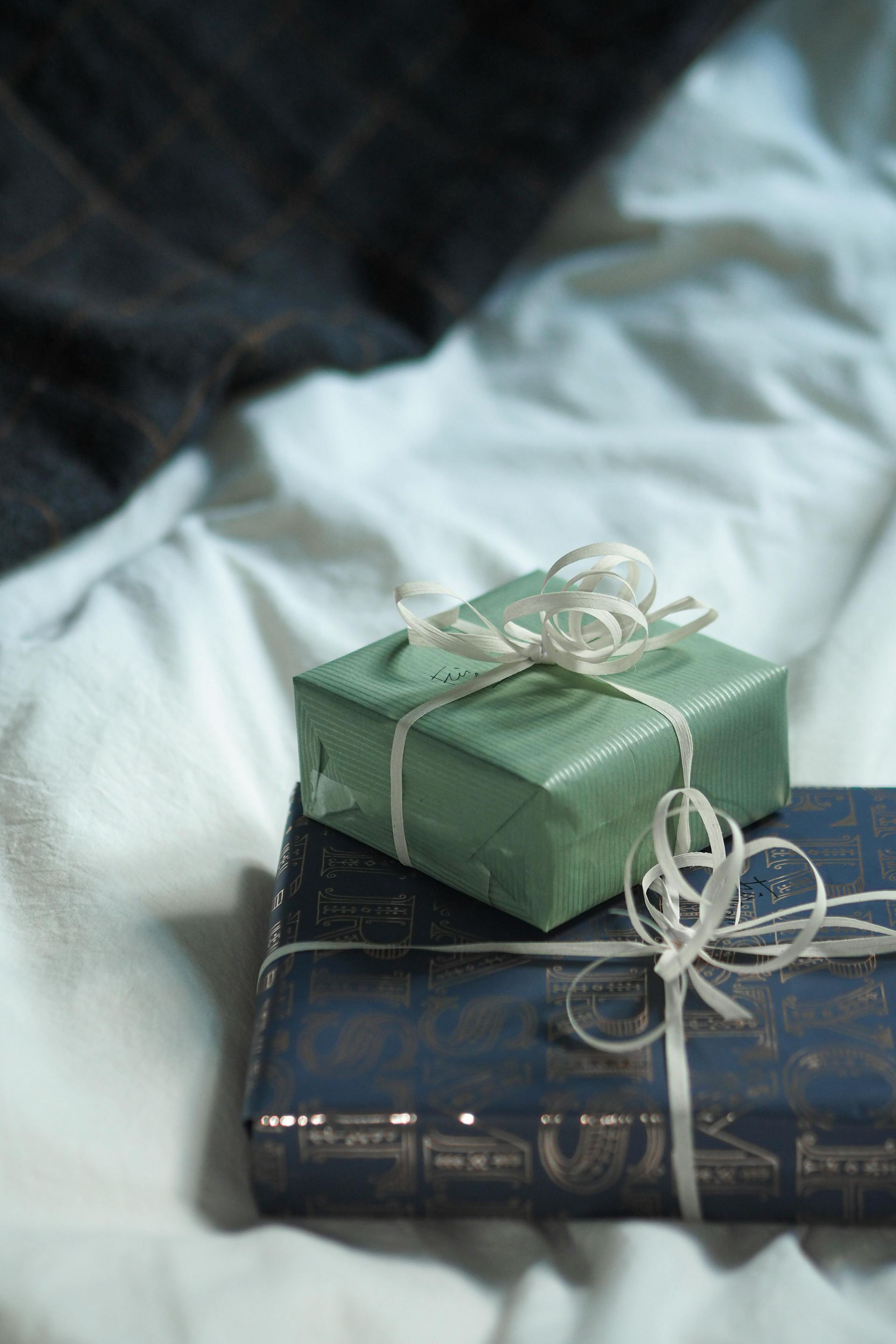 Two wrapped gifts on a white bed. One is green, the other blue, tied with white ribbon.