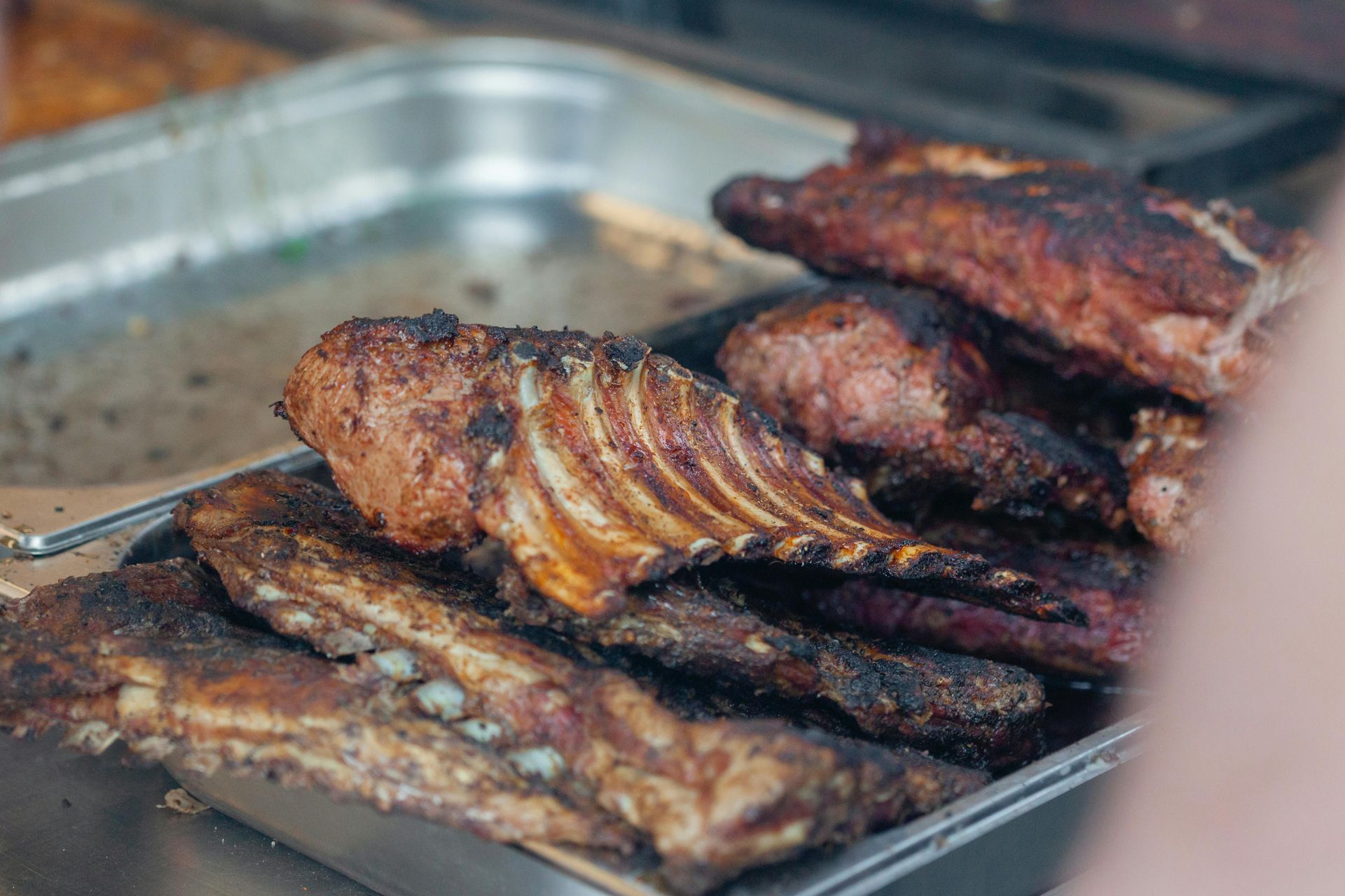 A metal tray filled with various cuts of grilled, browned, and charred meat ribs.