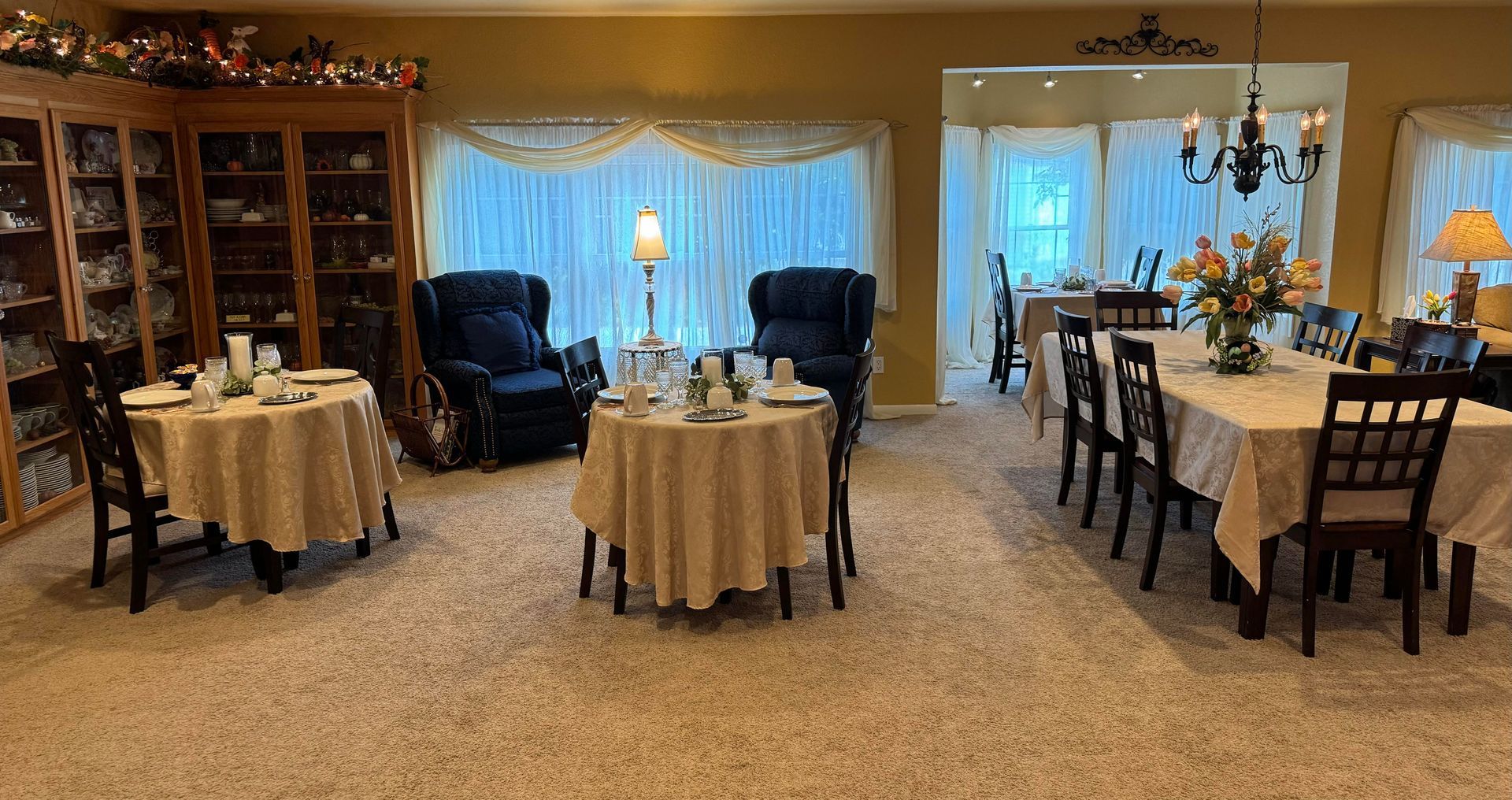 A carpeted dining room featuring two small round tables and a long rectangular table, all set for meals.