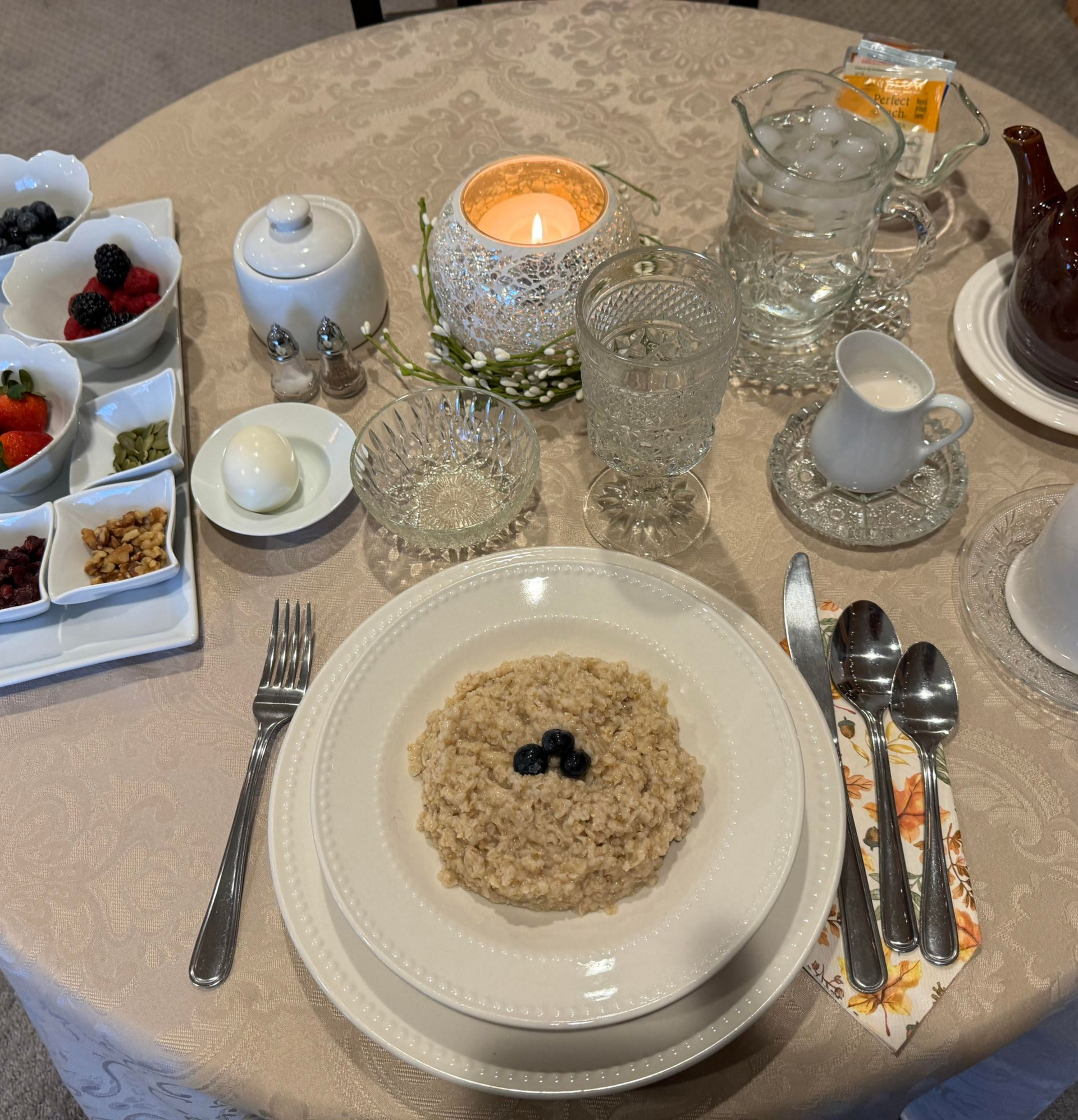 A place setting for a breakfast meal featuring a bowl of oatmeal with berries, sides of fruit, nuts, and a soft-boiled egg.