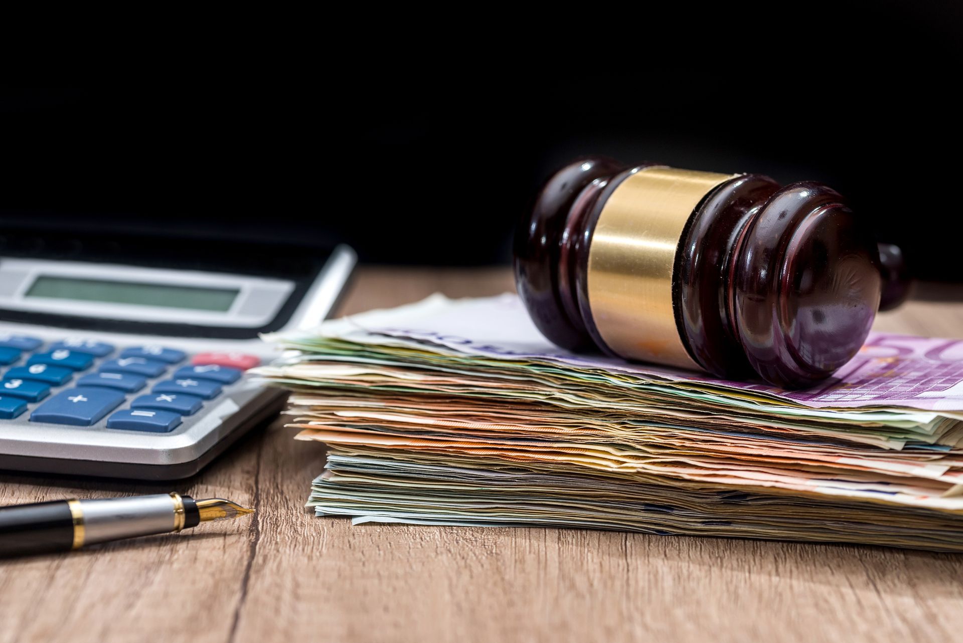 A judge 's gavel is sitting on top of a pile of money next to a calculator and pen.