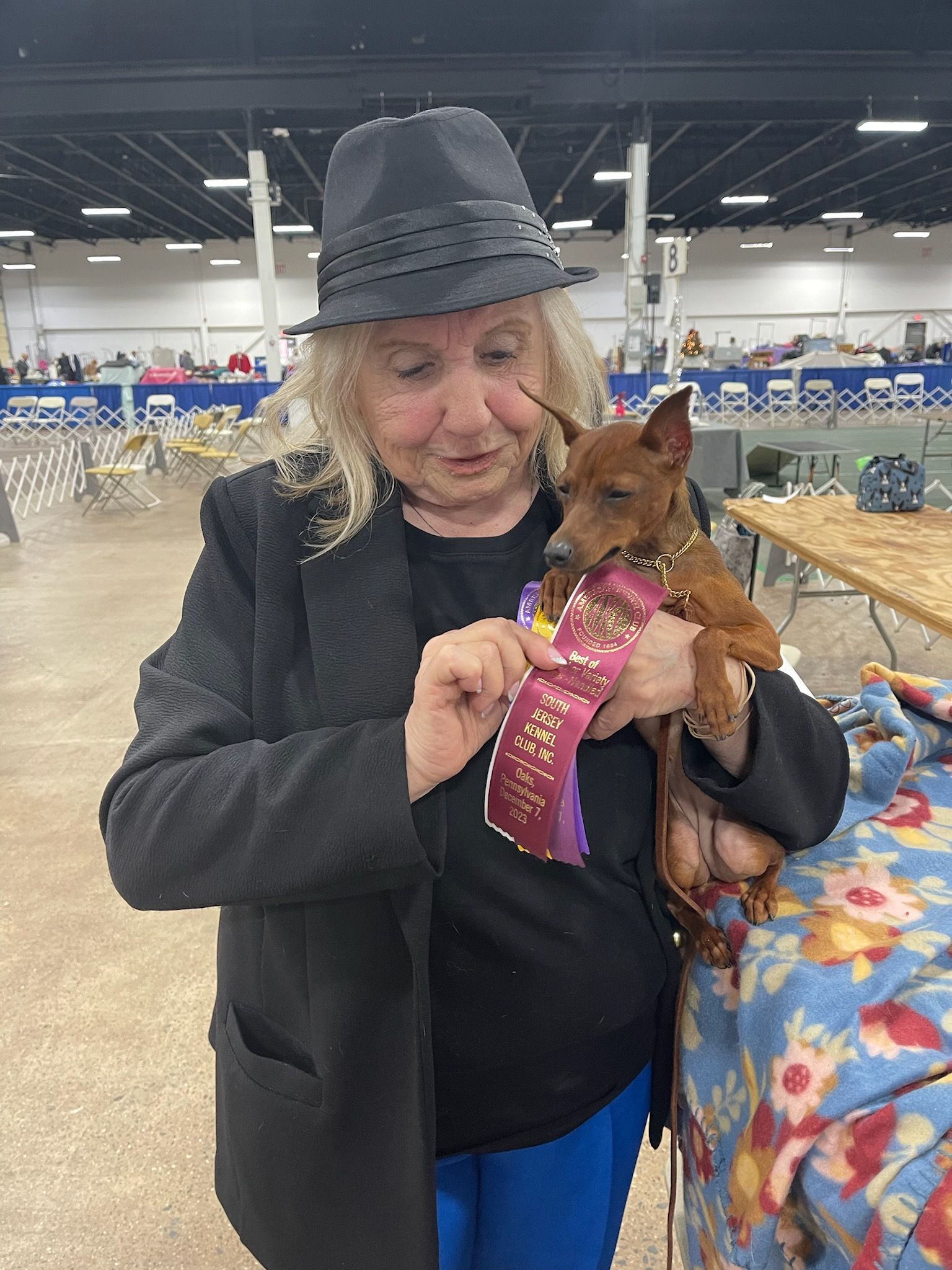 A woman is holding a small dog with a ribbon around its neck.