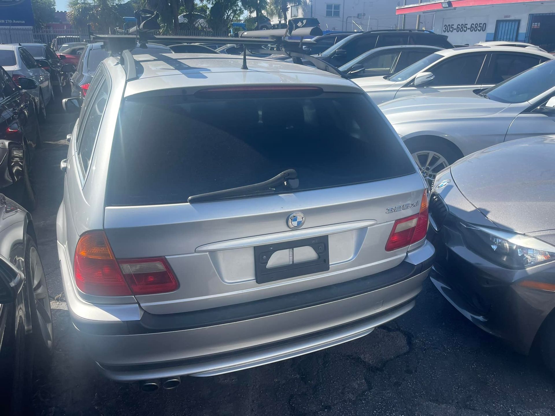 A silver bmw is parked in a lot with other cars.