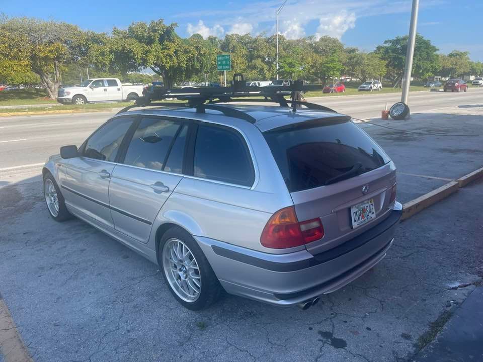 A silver bmw with a roof rack is parked in a parking lot.