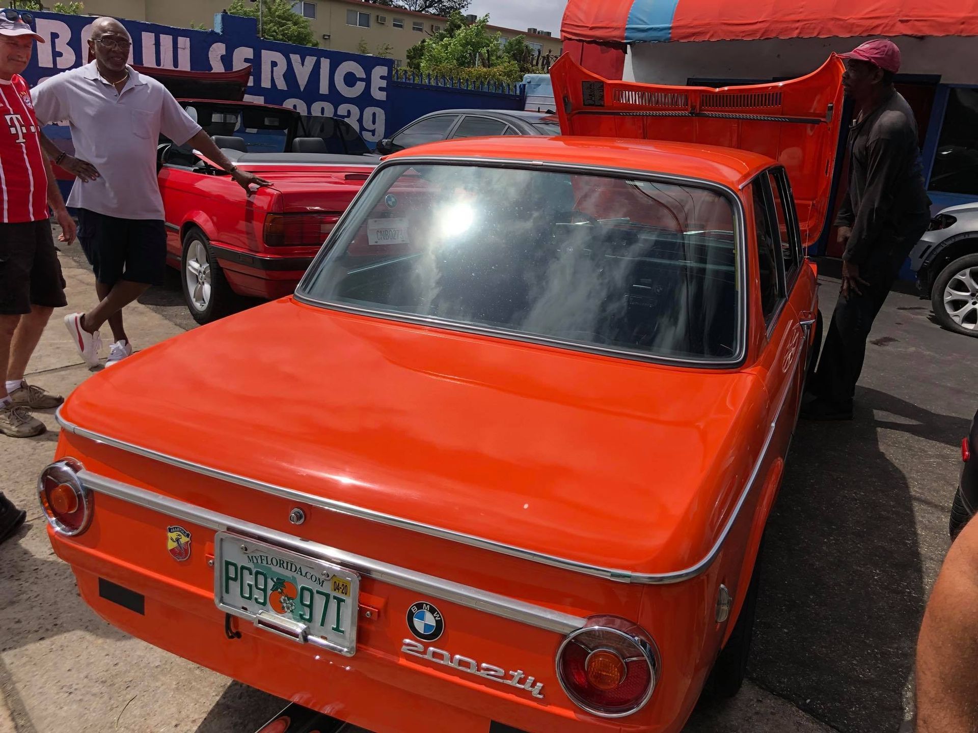 A man is opening the hood of an orange bmw