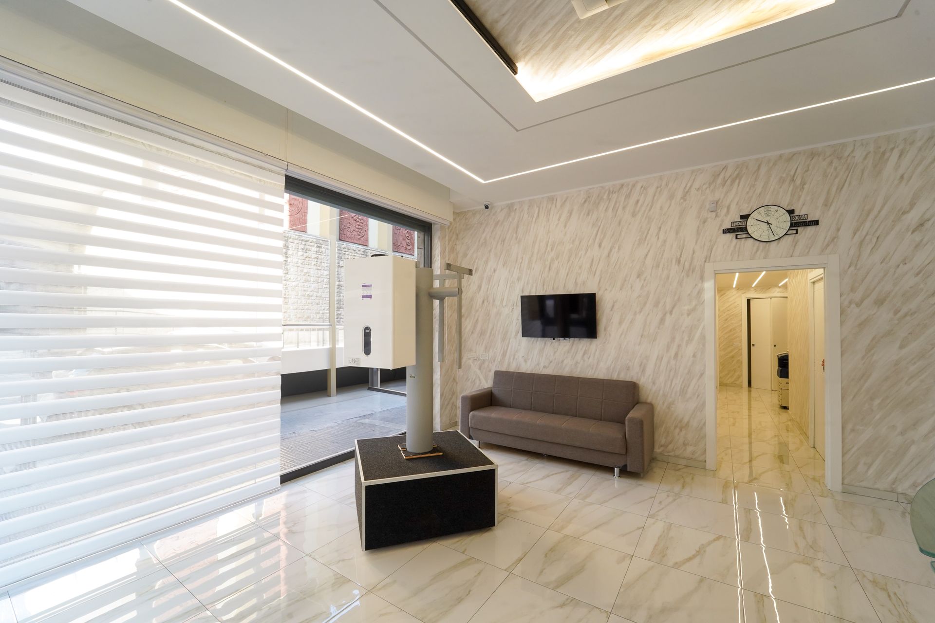 Moderna sala d'attesa con divano, TV, pareti decorative testurizzate e pavimento chiaro.