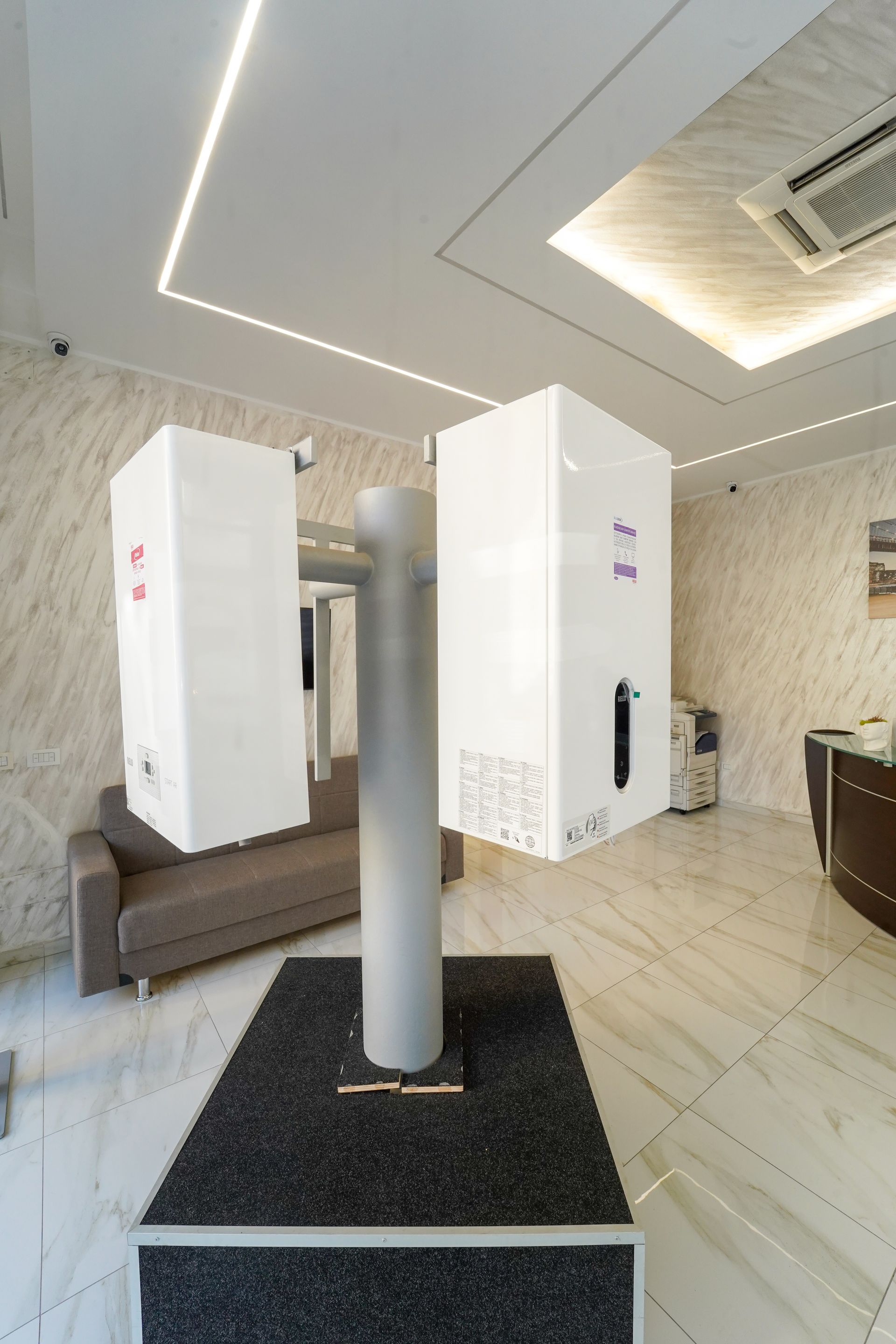 Due macchine bianche su un palo in un ufficio, posizionate sopra un tappeto nero su un pavimento in marmo.