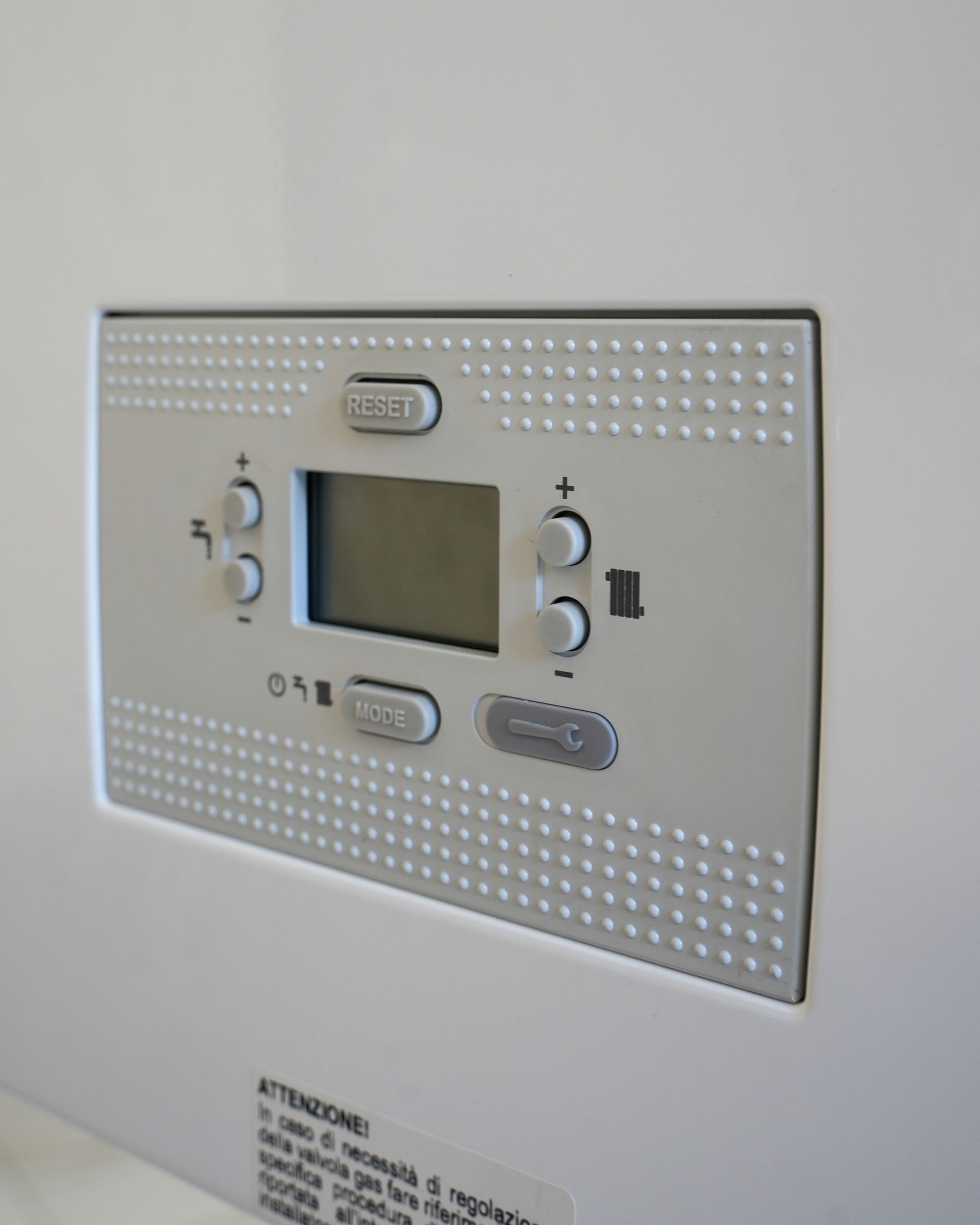 Pannello di controllo bianco con pulsanti e display su una superficie bianca, possibilmente per una caldaia o un impianto di riscaldamento.