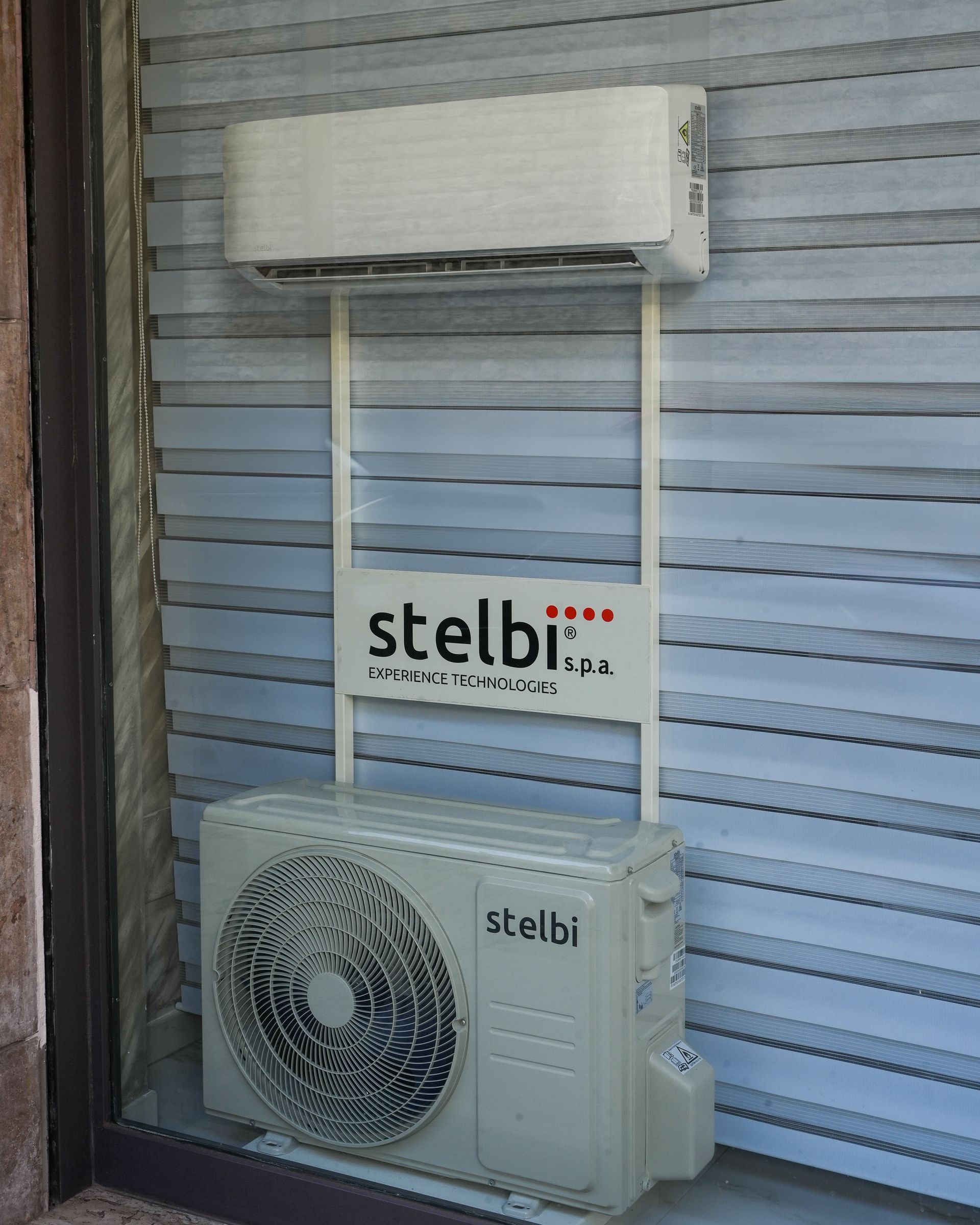 Esposizione di un condizionatore in vetrina. Unità interna bianca sopra un'unità esterna bianca, con la scritta 