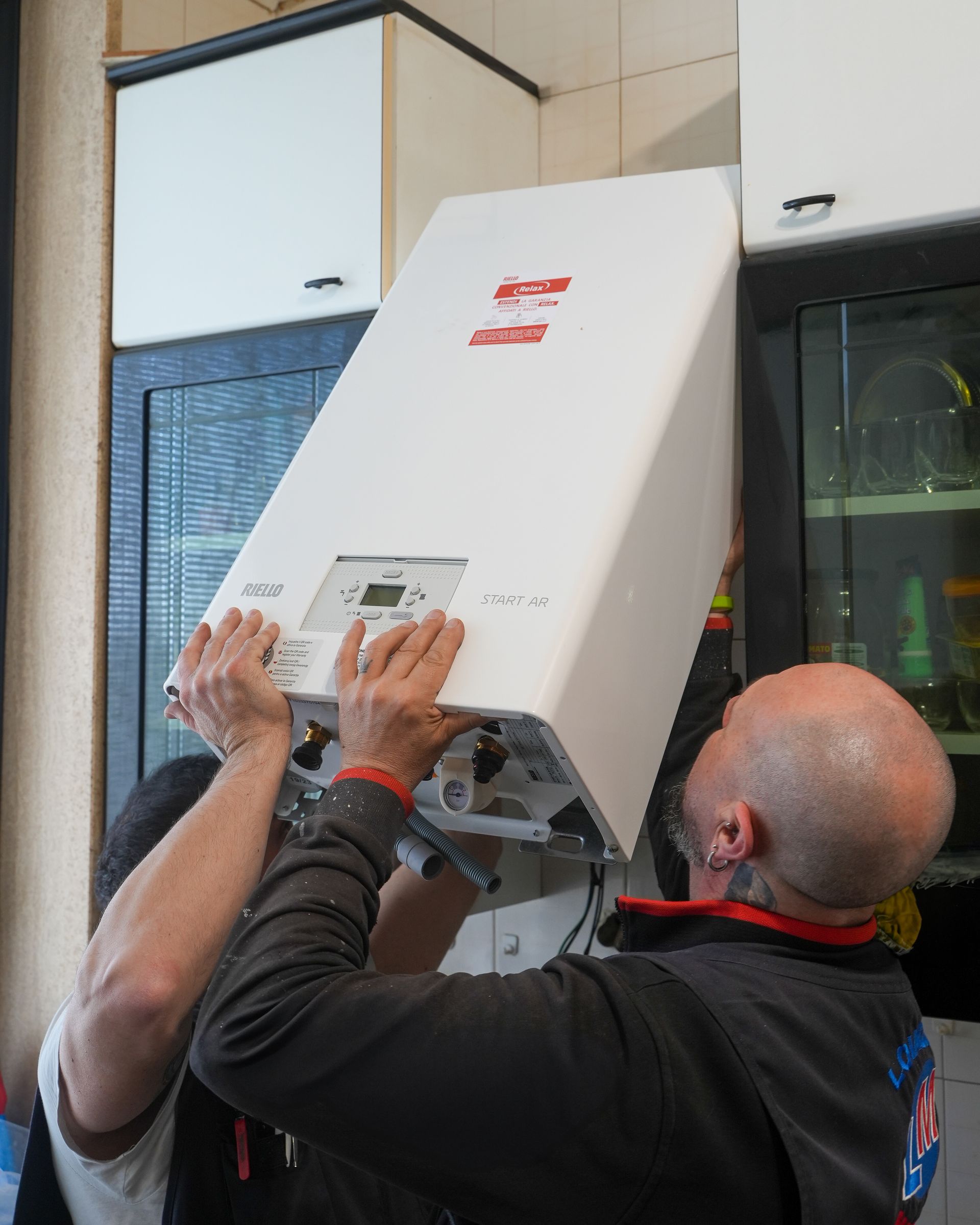 Due persone installano una caldaia bianca a parete in una cucina, tenendola sollevata.