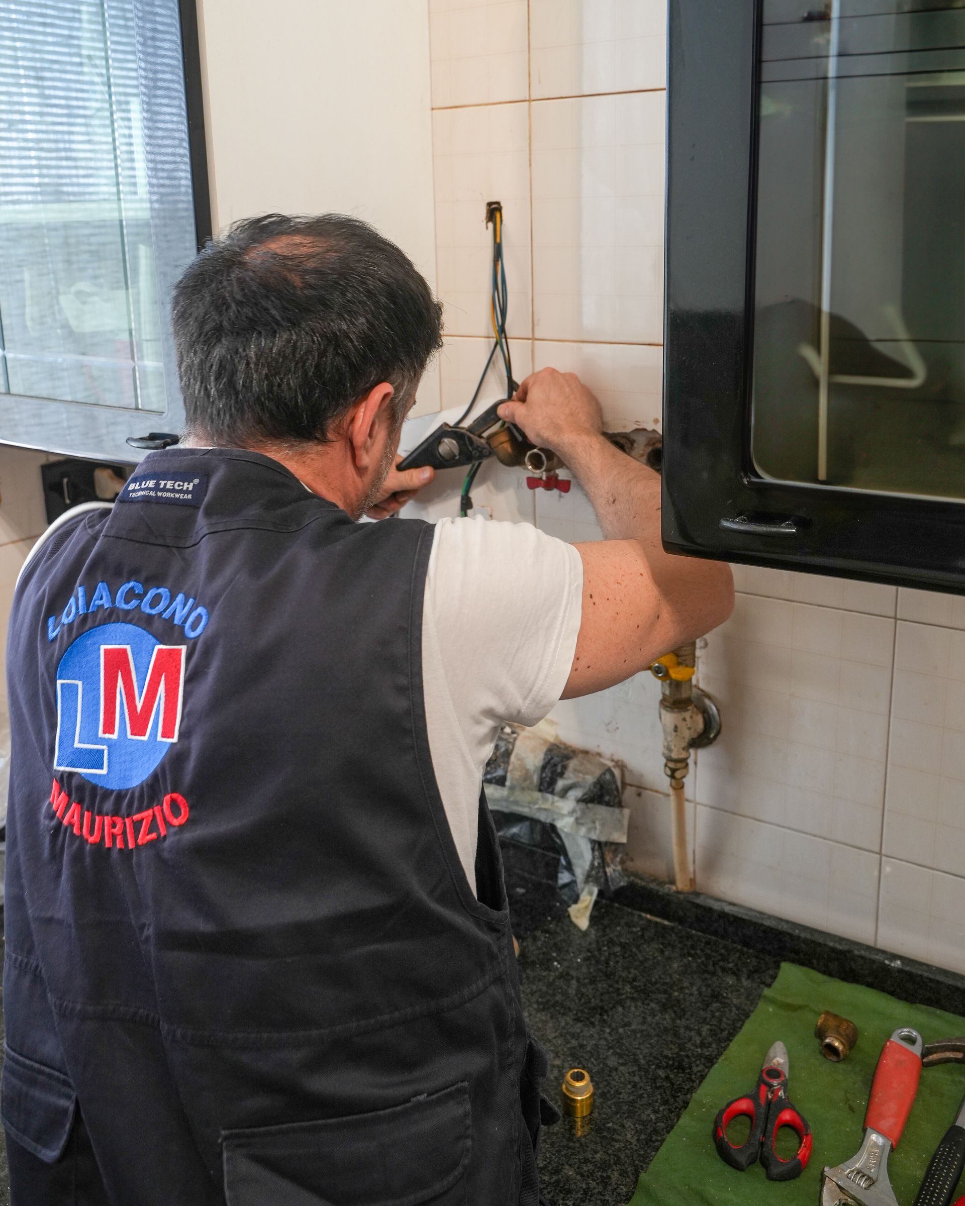 Idraulico che lavora sui tubi del gas in una cucina, indossando un gilet blu navy.