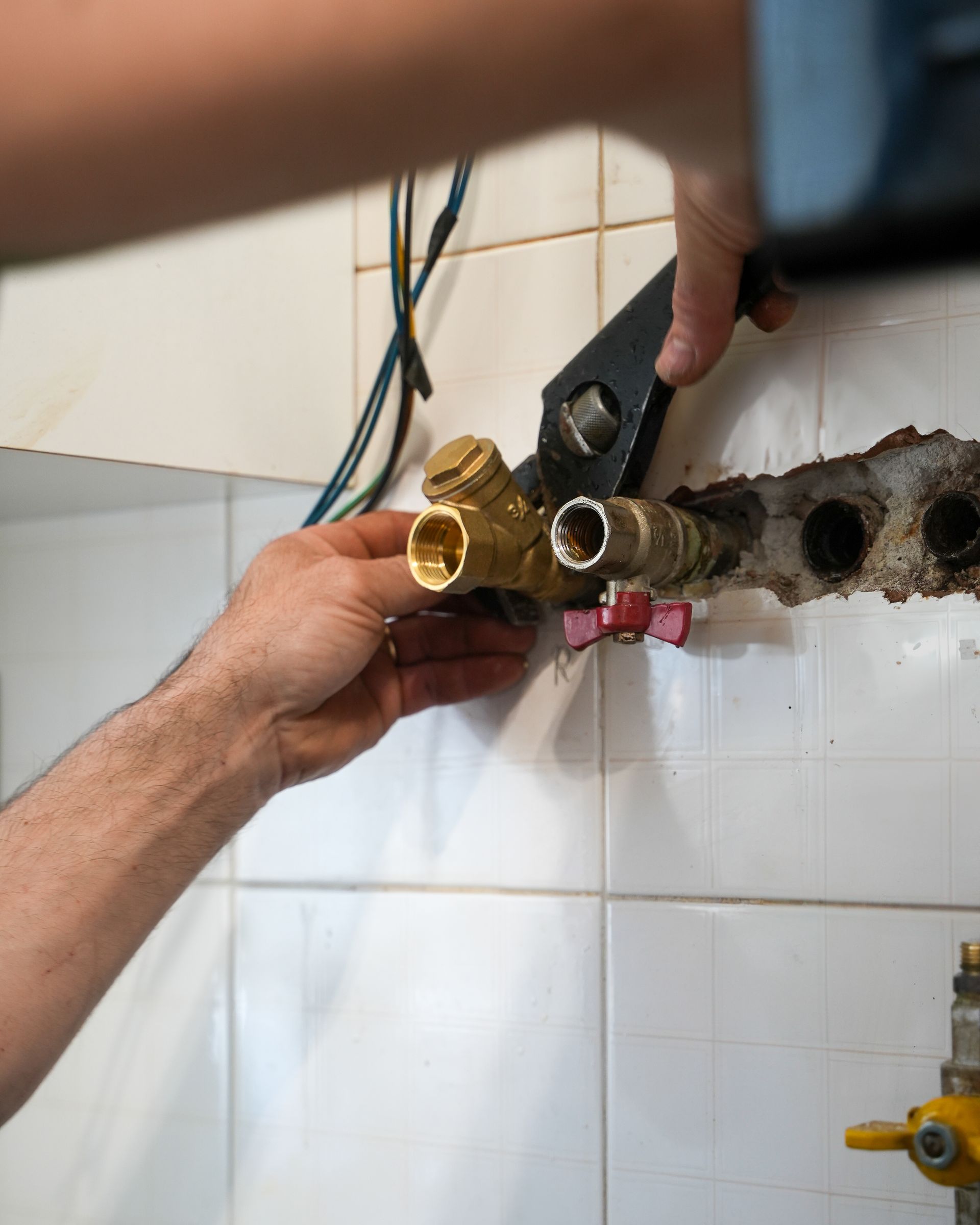Persona che utilizza una chiave inglese per serrare i raccordi idraulici su una parete piastrellata.