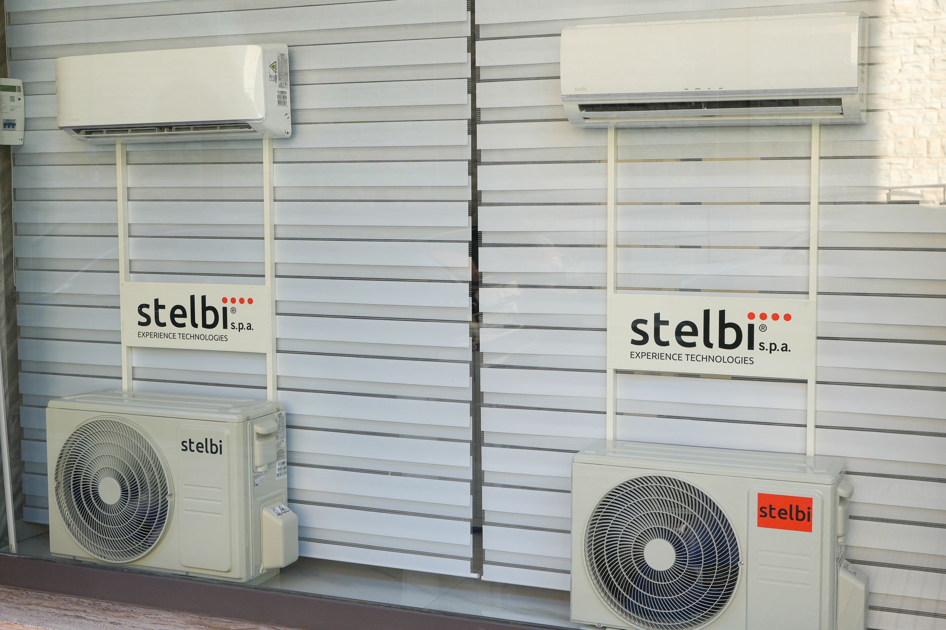 Due unità di aria condizionata montate su una parete ondulata bianca, con unità esterne sottostanti, marchiate 