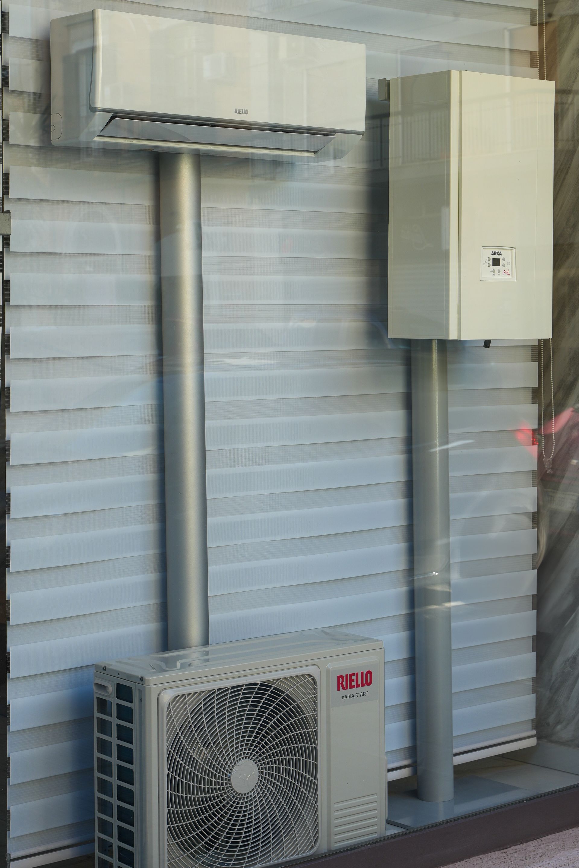 Un sistema di aria condizionata e una caldaia a gas montati su pali contro una finestra con persiane.