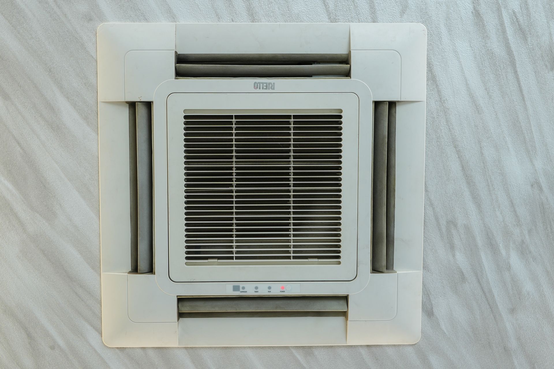 Unità di aria condizionata bianca montata a soffitto con bocchette e griglia in un soffitto bianco.