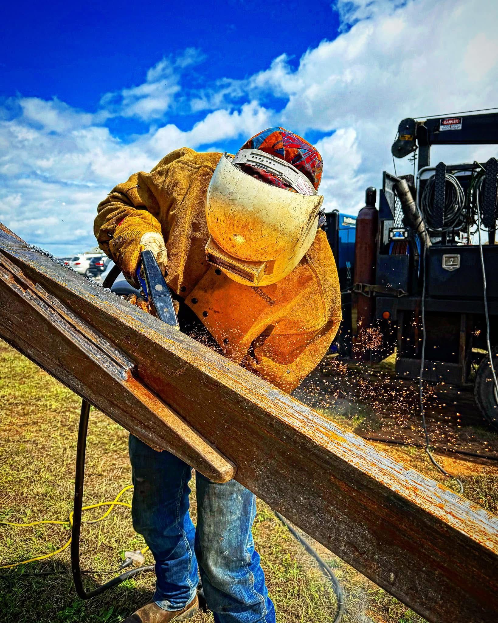 Welder in protective gear using a grinder outdoors. Restoration welding