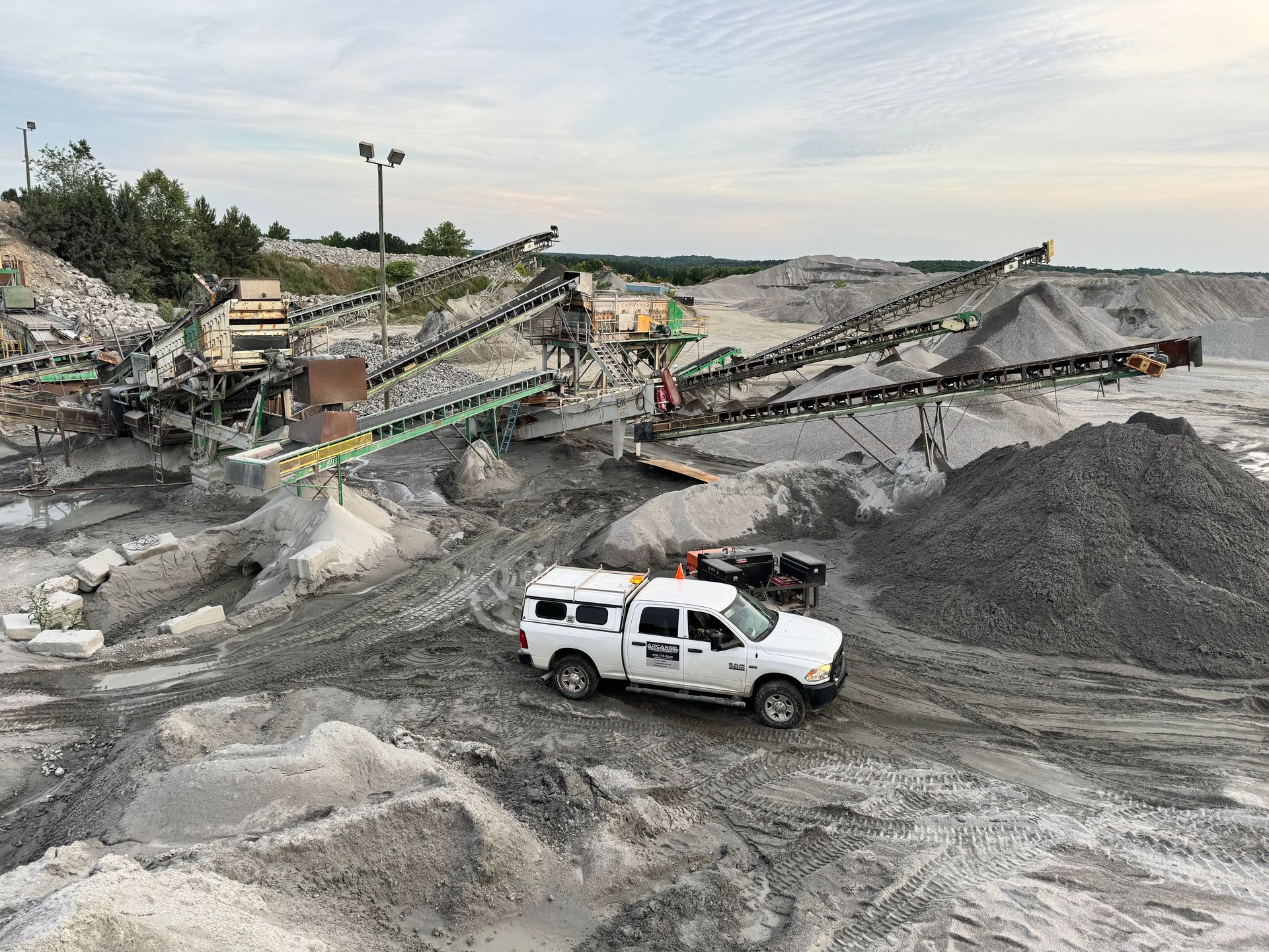 White truck on gravel in a quarry with conveyor belts sorting material. Mobile welder for heavy machinery