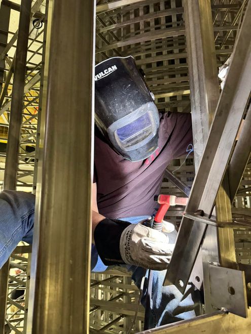 Welder wearing a helmet working on metal scaffolding with a torch. Oil and gas welding