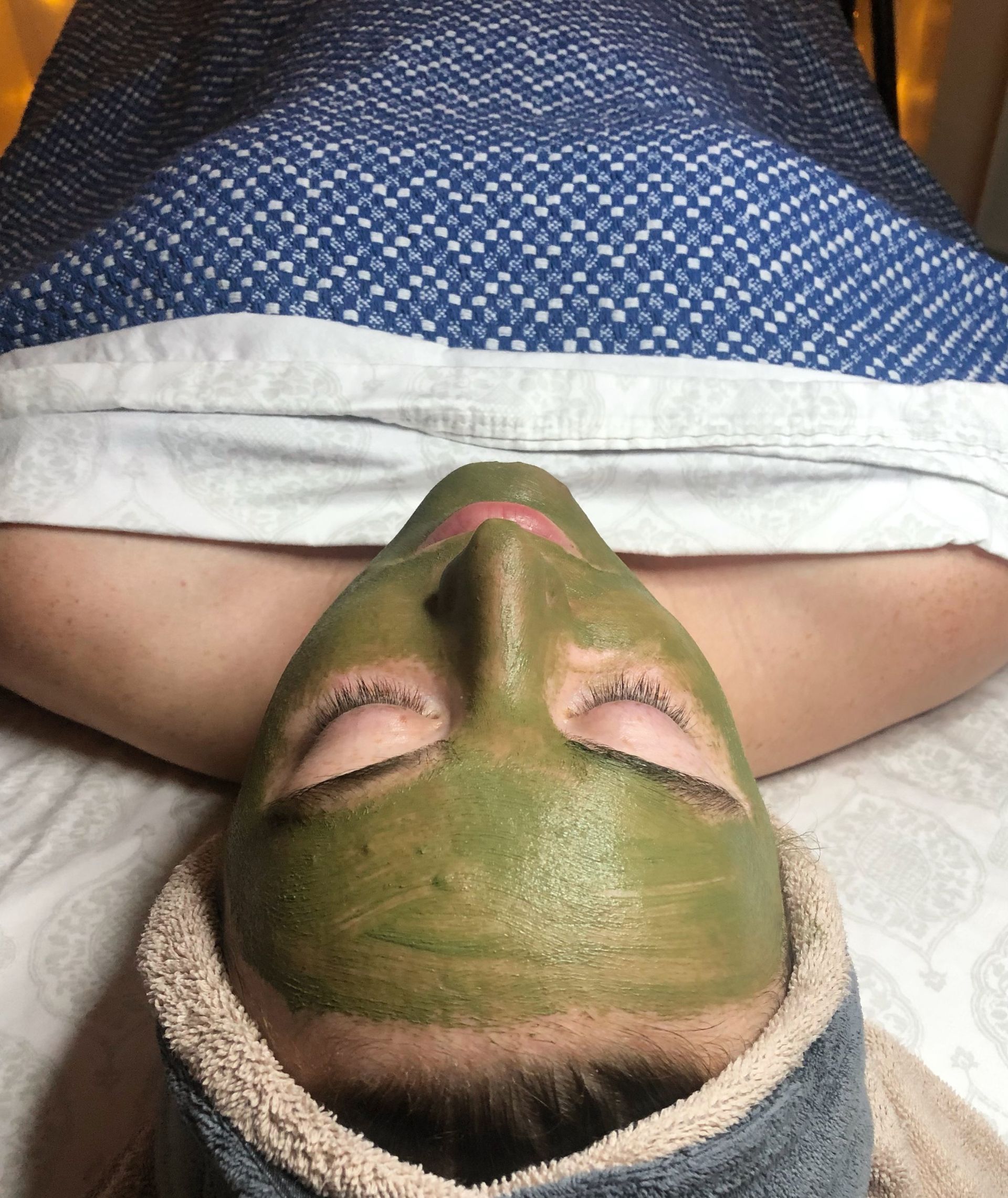 A woman is laying on a bed with a green mask on her face.